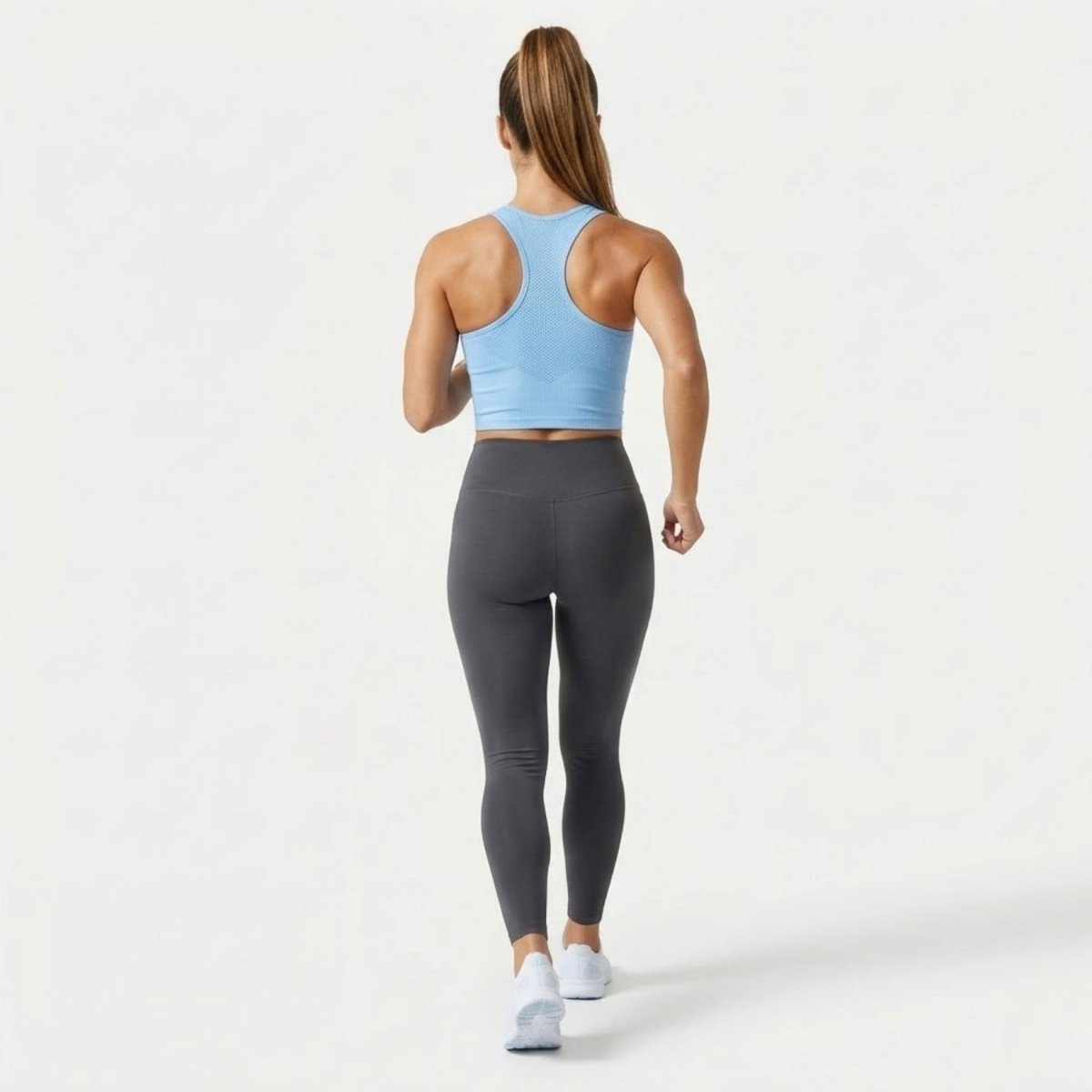 Woman walking away wearing light blue racerback activewear top showing back design