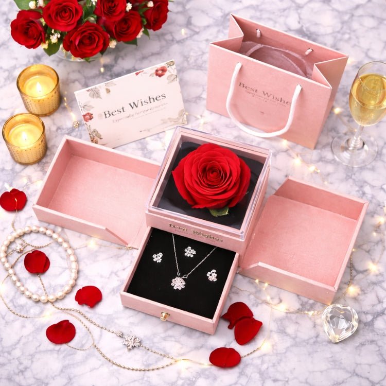 Romantic gift set on a marble table including a preserved red rose box, gift bag, and greeting card, surrounded by rose petals, pearls, and soft candlelight
