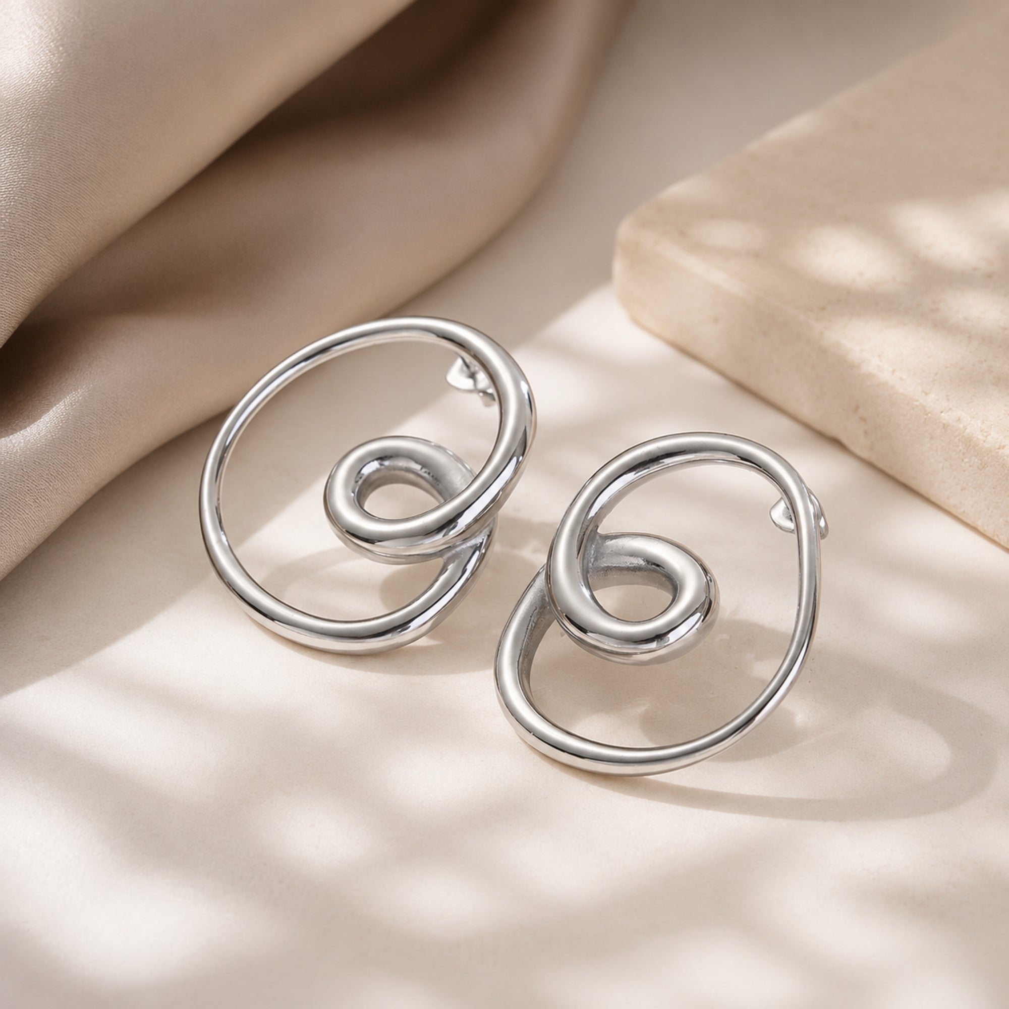 Close up of polished 925 sterling silver loop knot earrings lying flat on silk, displaying the reflective surface and intricate intertwined wire design.