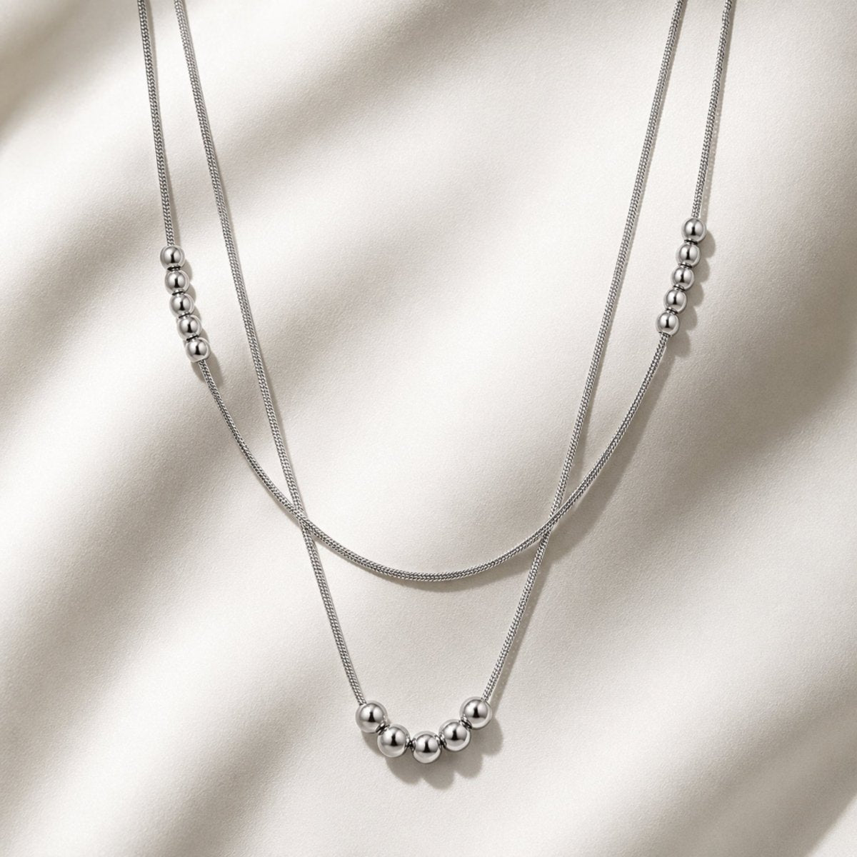 High resolution flat lay view of a silver double layered snake chain necklace showcasing smooth metal ball clusters and fluid dual chains.