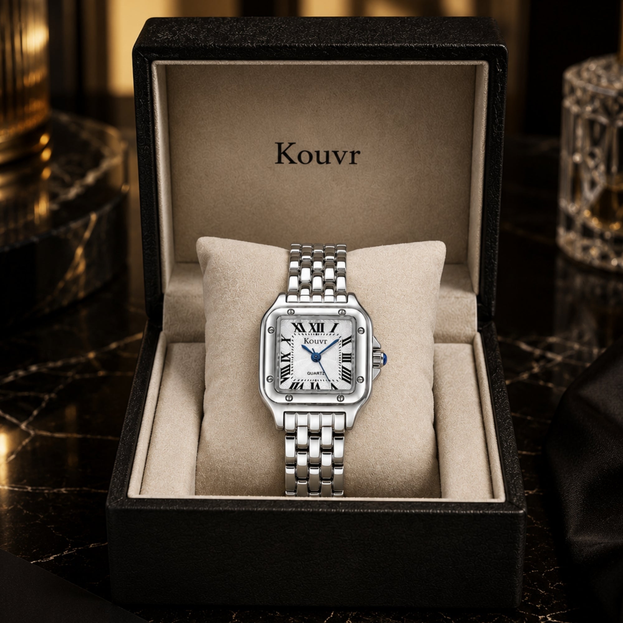 Kouvr women's elegant silver stainless steel square watch with blue hands and Roman numerals resting on a soft beige display pillow.