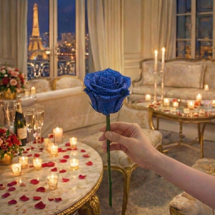 A hand holding a single, long-stemmed royal blue glitter rose. The artificial flower sparkles against a candlelit romantic background.