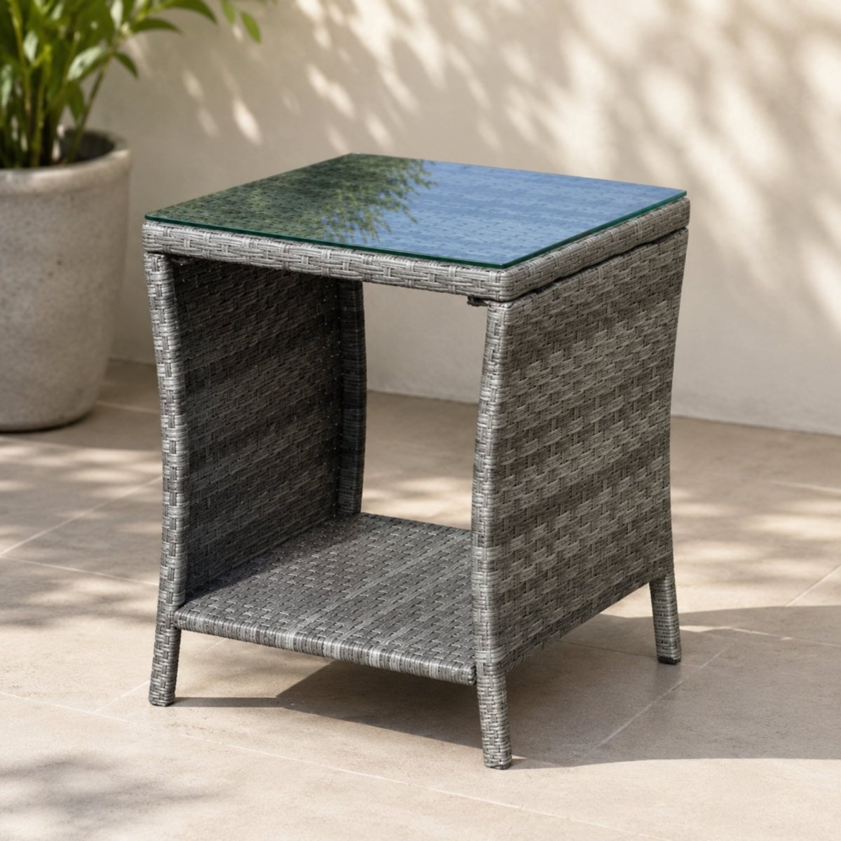 Empty square grey rattan patio end table showing the woven texture, glass surface, and sturdy leg design in an outdoor setting.