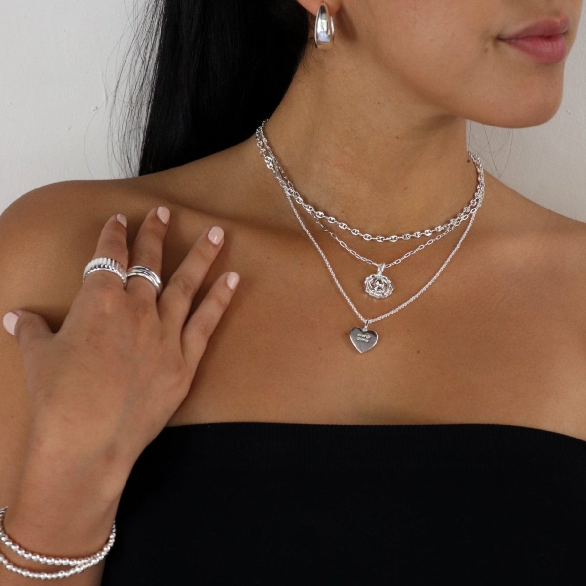 Woman wearing silver jewelry including necklaces, rings, and earrings on a neutral background