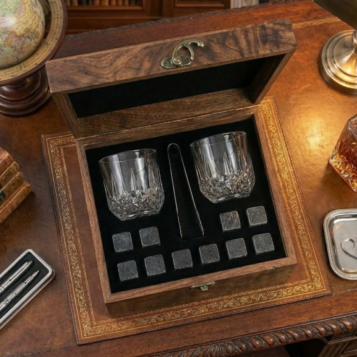 An overhead view of the Kouvr whiskey gift set, highlighting the two crystal-cut glasses, tongs, and eight granite chilling stones inside the wooden box.