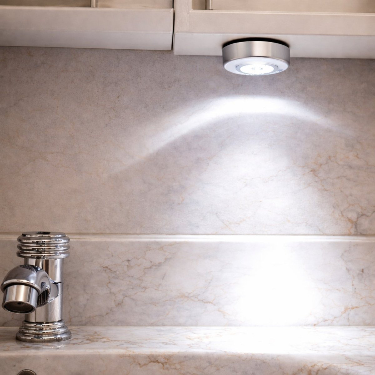 Kouvr stick-on LED light mounted under white cabinetry illuminating marble countertop and chrome faucet with bright cool white light.