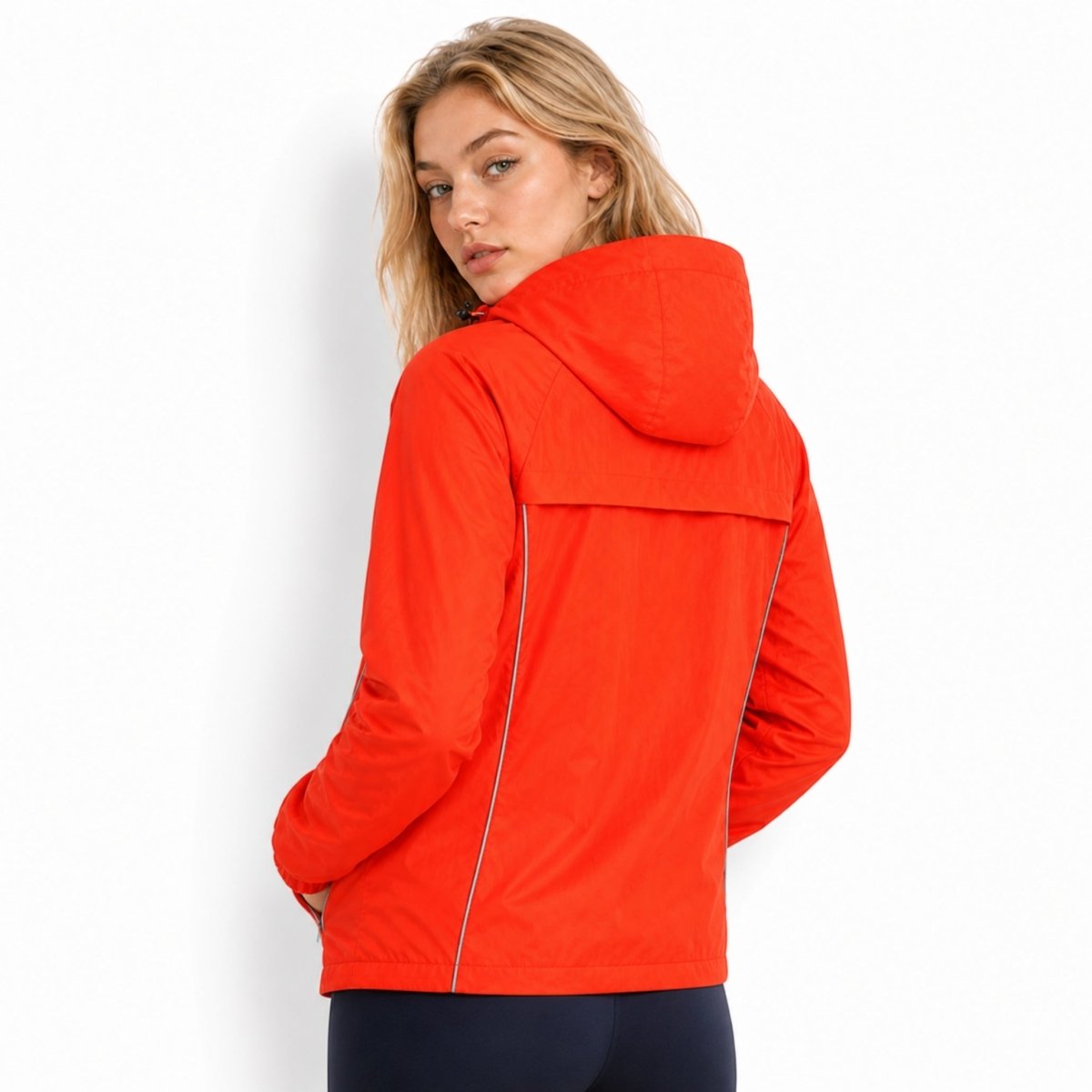 Back view of woman wearing Kouvr bright orange hooded running jacket featuring a structured back yoke and reflective safety piping.