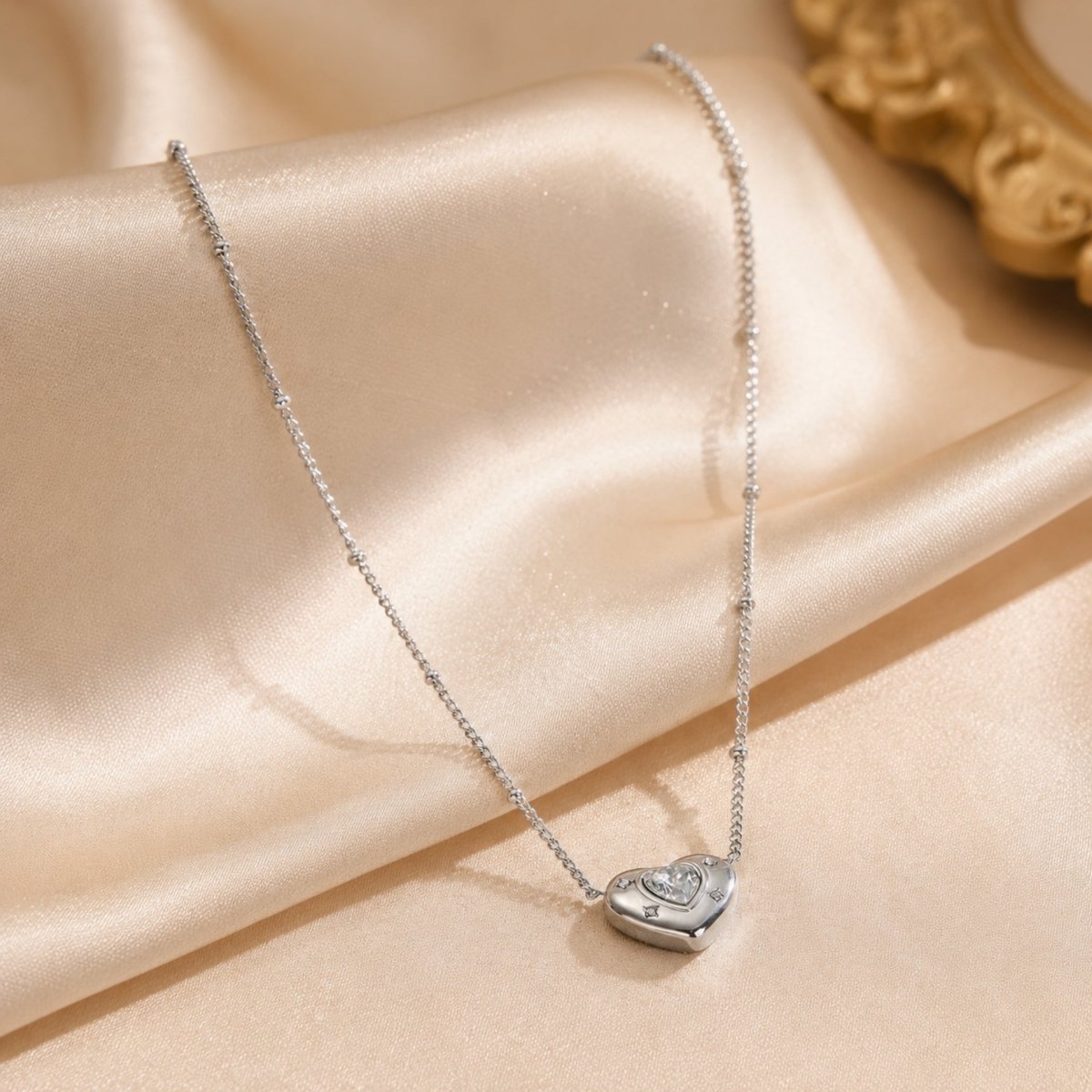 Elegant silver heart necklace by Kouvr gracefully laid out on champagne silk fabric highlighting its brilliant shine.