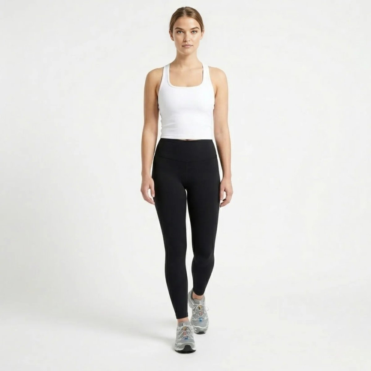 Full body shot of model in white sleeveless workout crop top, black leggings, and running shoes.