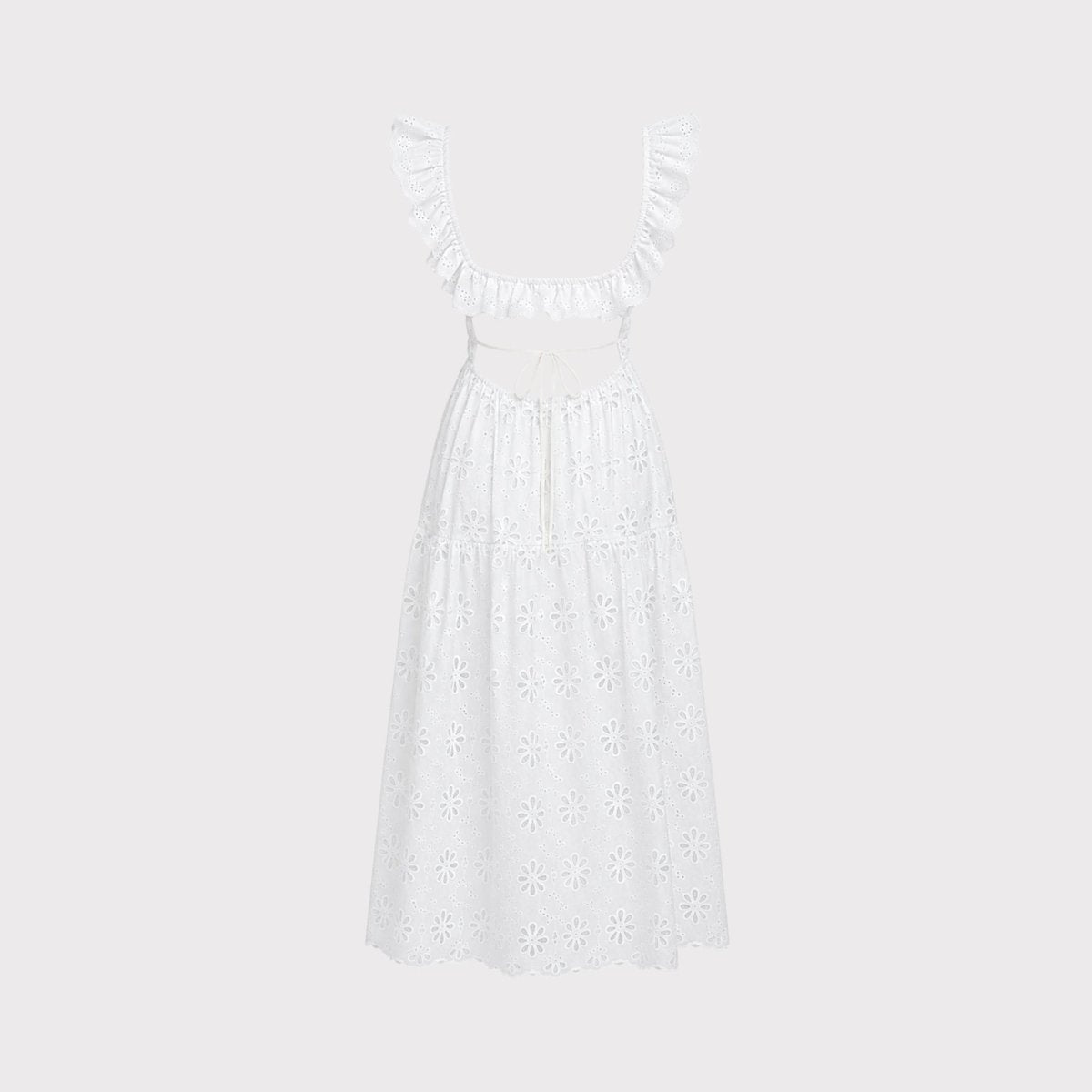 Studio shot detailing the back view of a white open back tie dress with intricate eyelet floral embroidery on a light grey background.