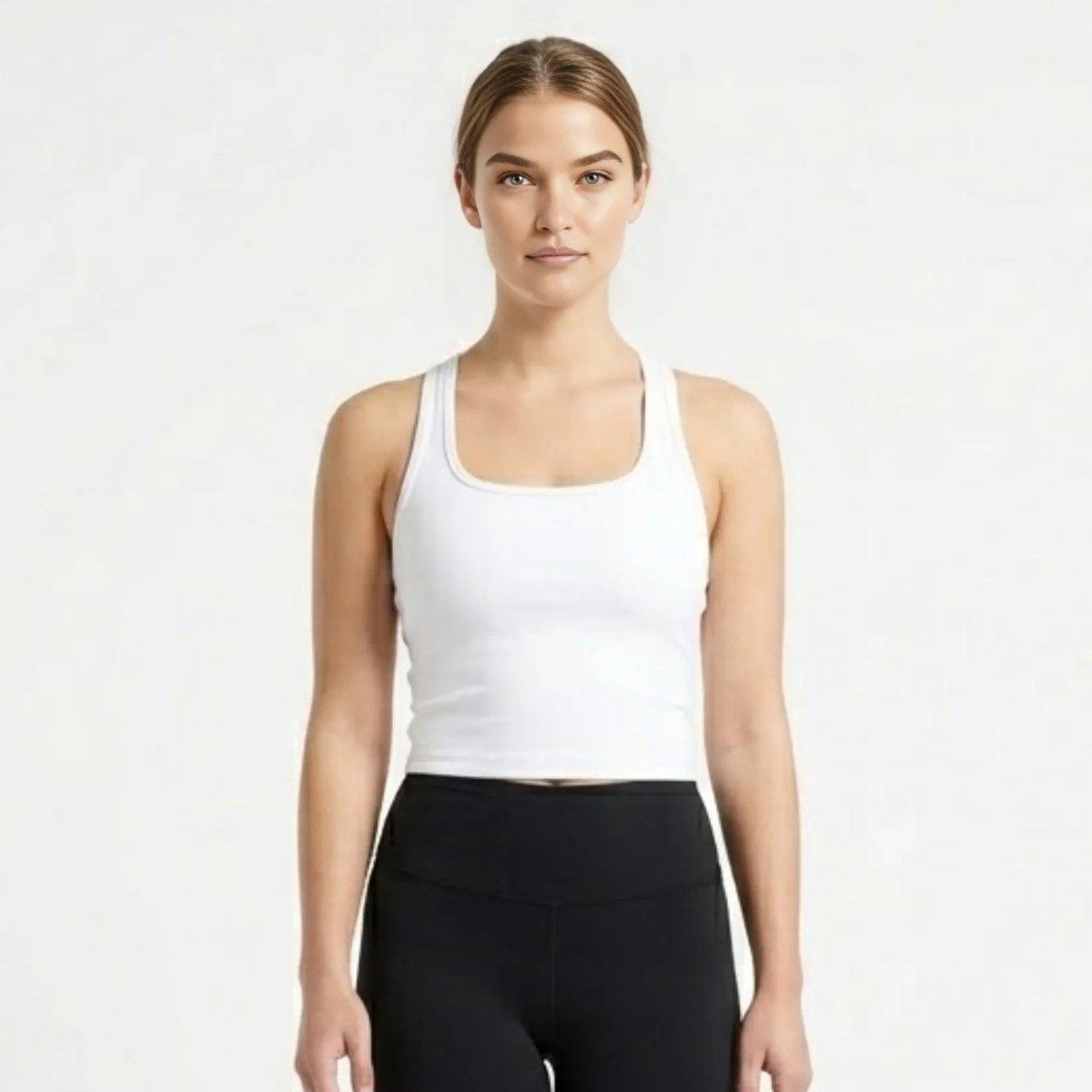 Woman wearing a luxury white ribbed racerback crop tank top with black leggings facing forward.