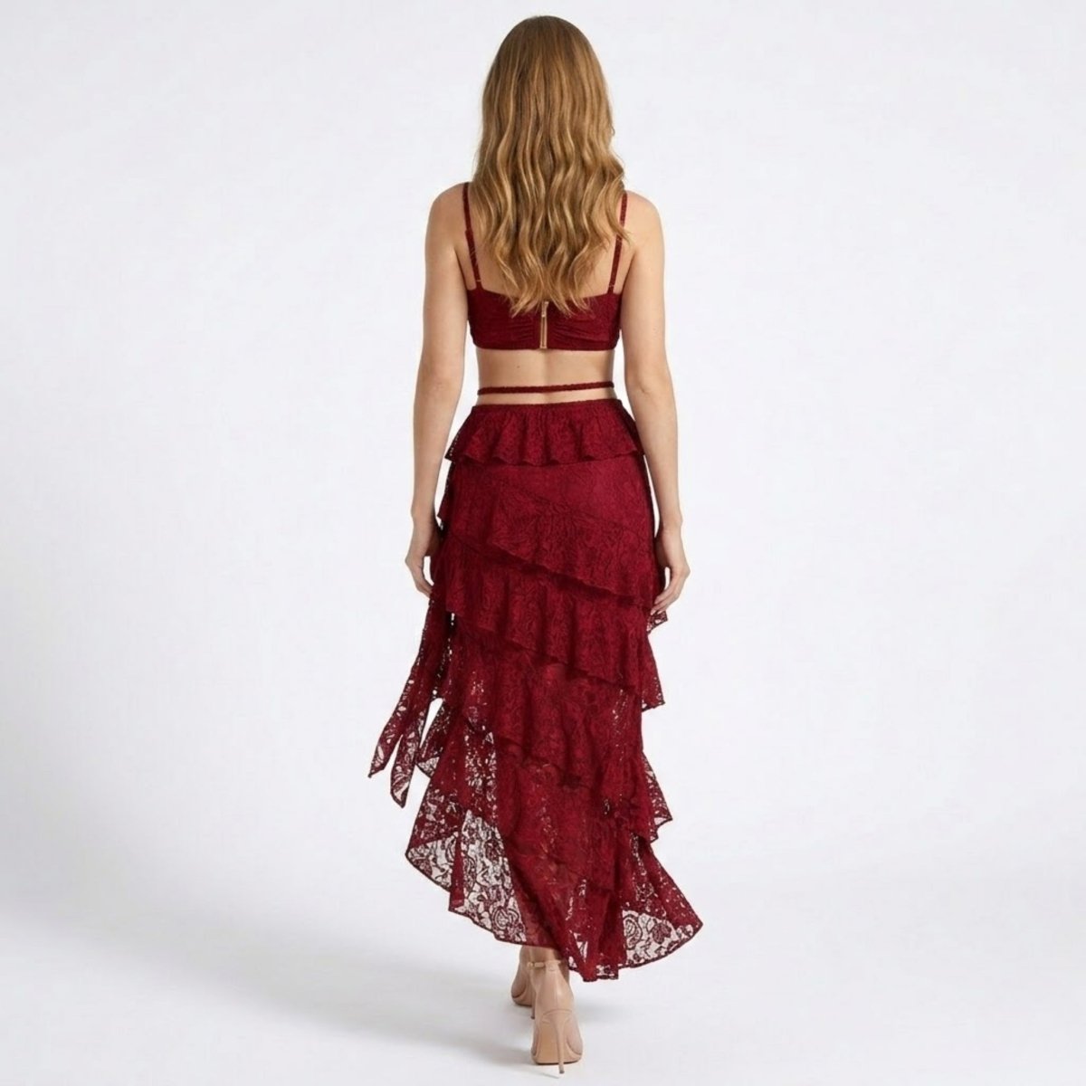Back view of a wine red lace two piece skirt set showcasing an exposed gold back zipper on the crop top and cascading ruffles on the sheer lace train.