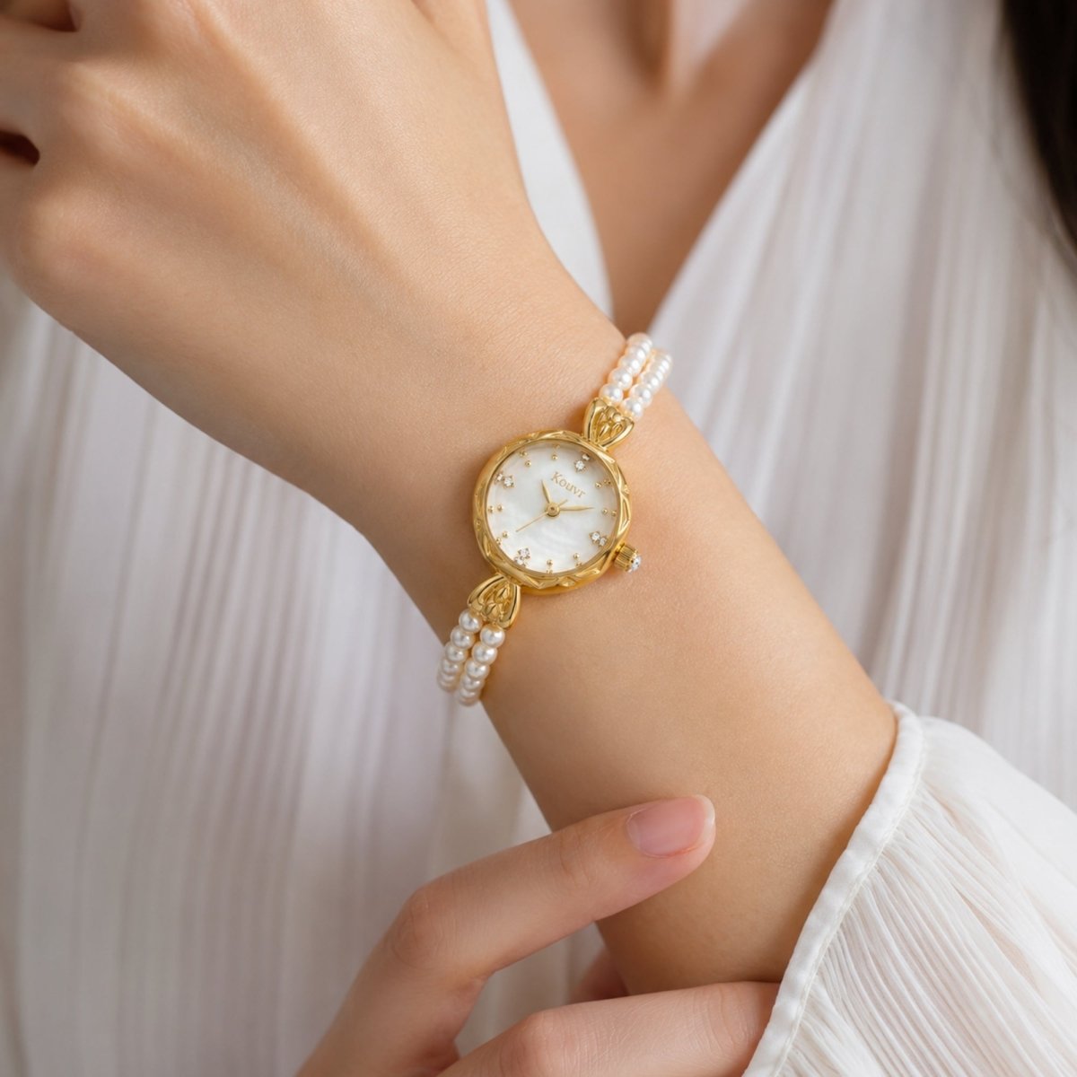 Woman wearing an elegant Kouvr gold and pearl bracelet watch on her wrist with a pleated white blouse.