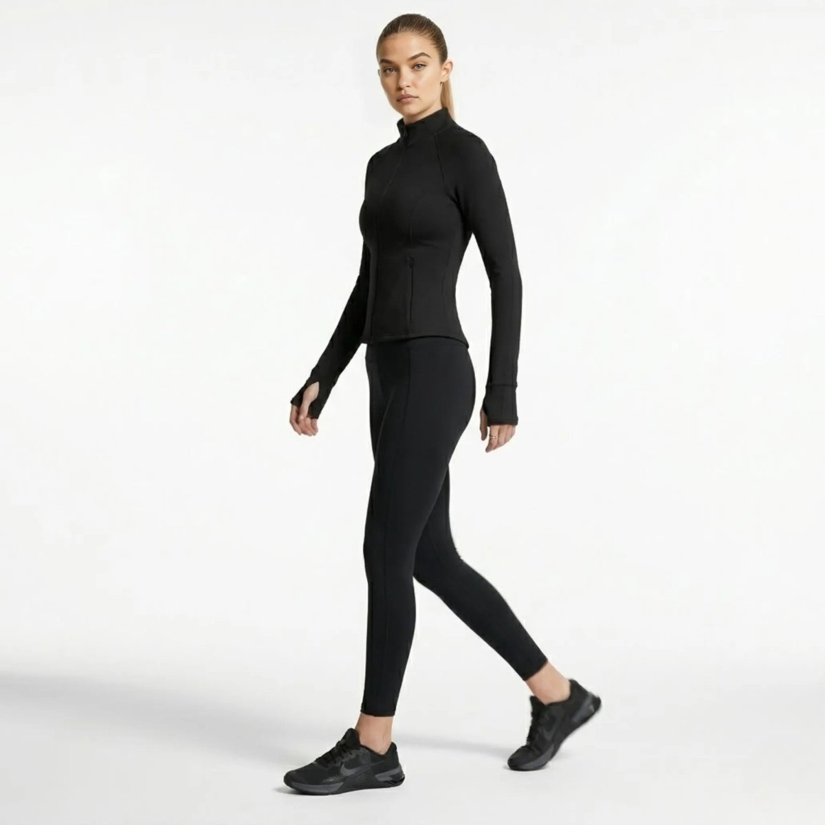 Side profile of woman walking in premium black activewear zip-up jacket highlighting fitted silhouette.