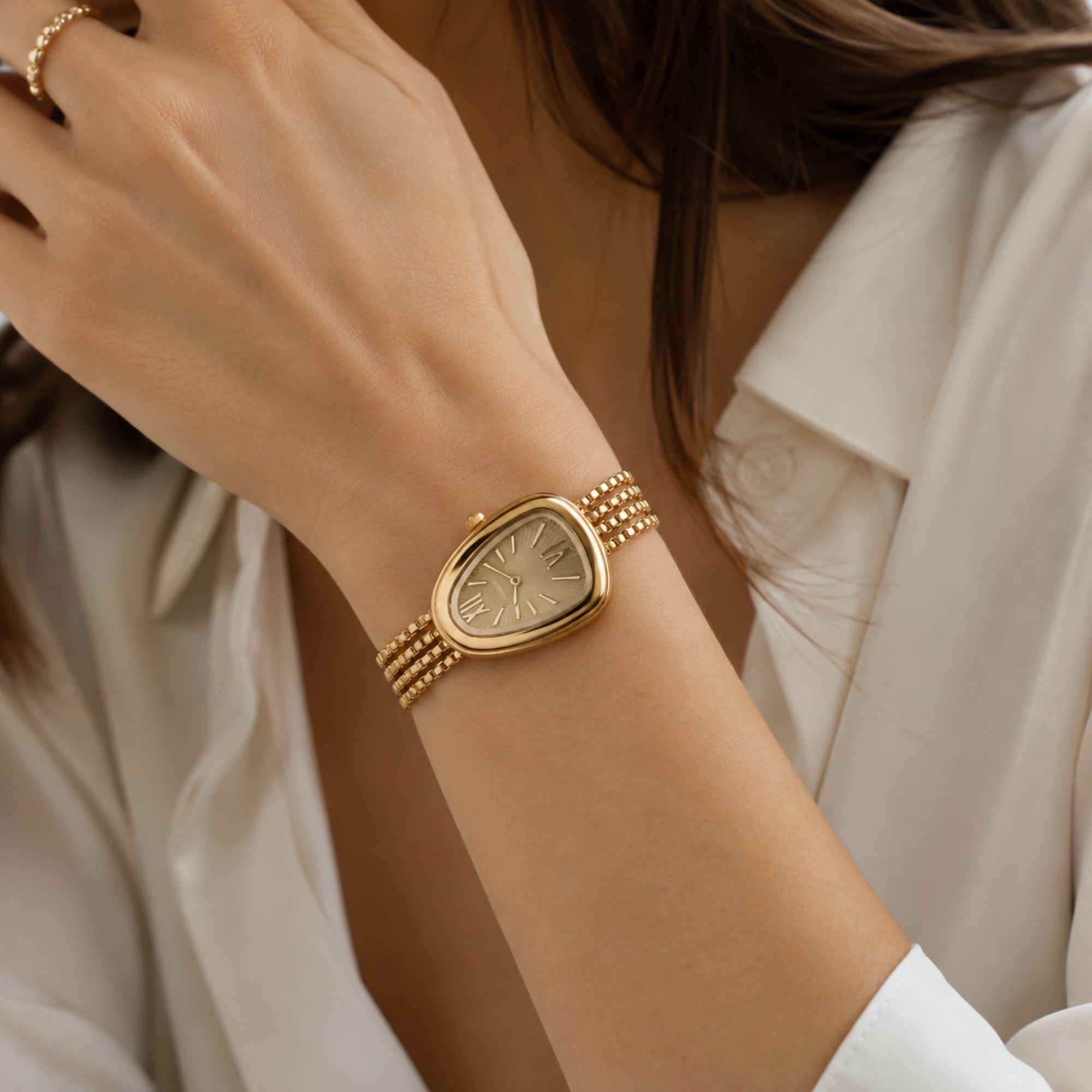 Close up of a woman wearing the Kouvr gold multi-strand bracelet watch paired with a white silk shirt, showcasing vintage luxury style.