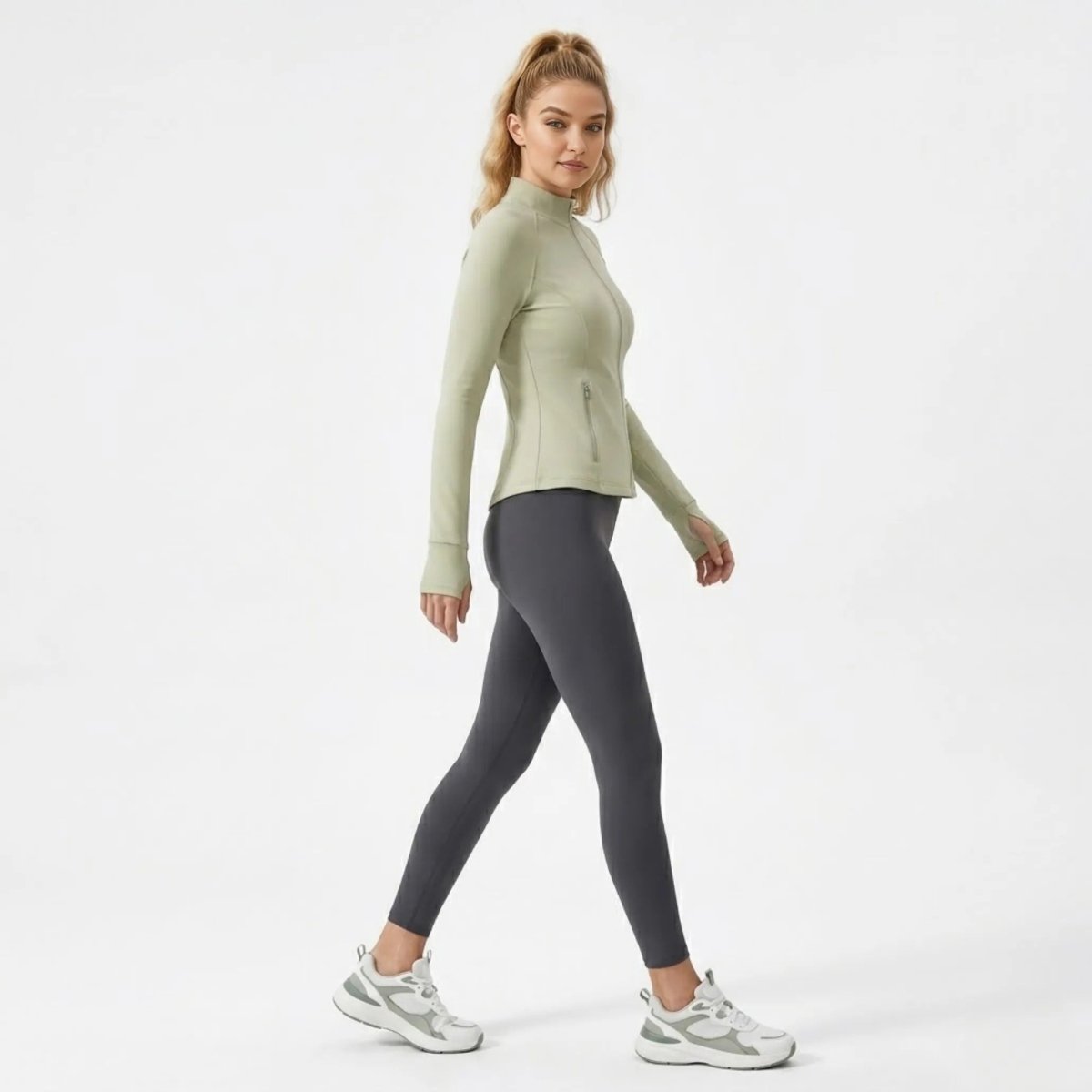 Side profile of woman walking in a stretchy fitted green athletic jacket with zippered pockets.