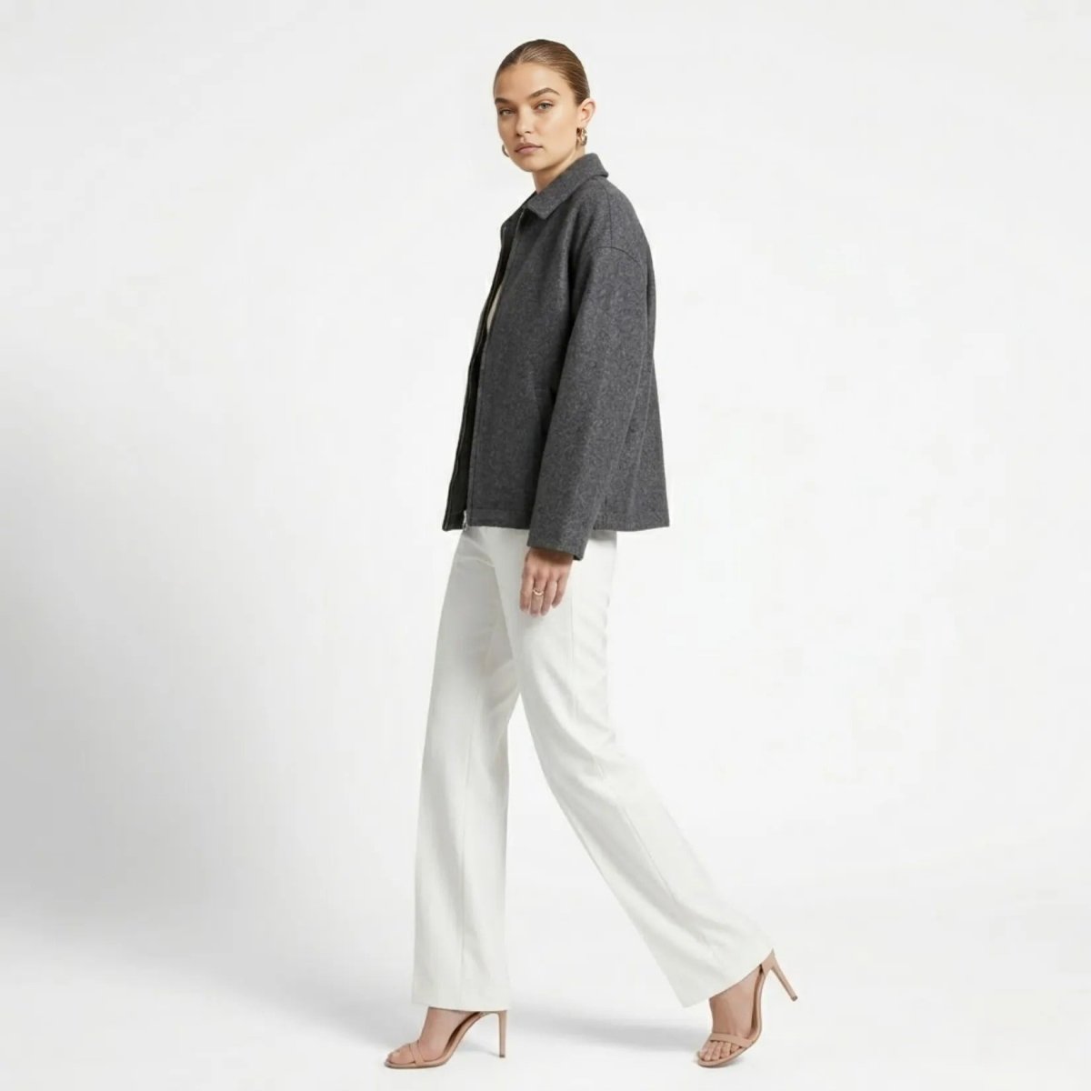 Side profile of female model walking in a grey cropped transitional wool zip jacket by Kouvr showing the relaxed sleeve fit.