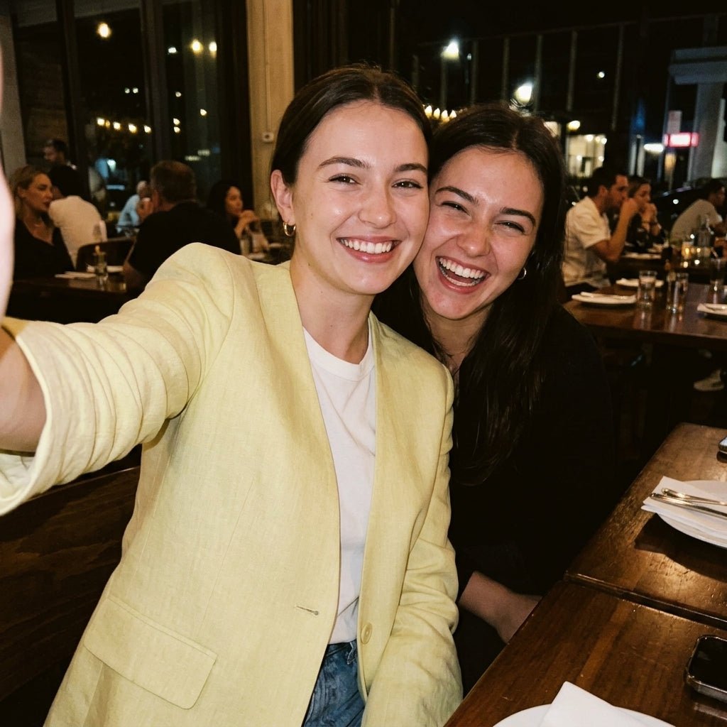 Smiling woman wearing Kouvr yellow linen blazer at a restaurant with a friend.