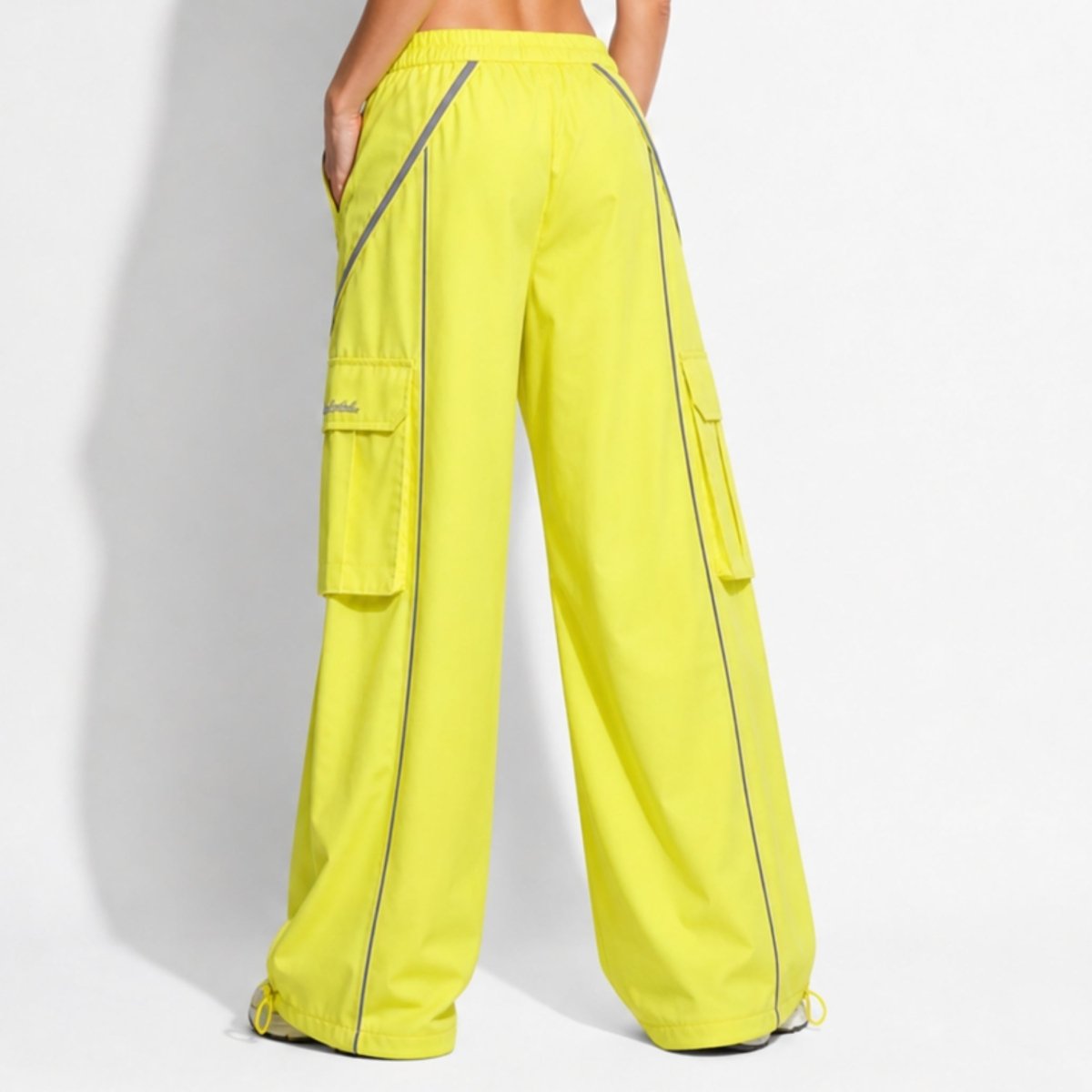 Back view of women's neon yellow baggy streetwear cargo pants showing reflective diagonal details