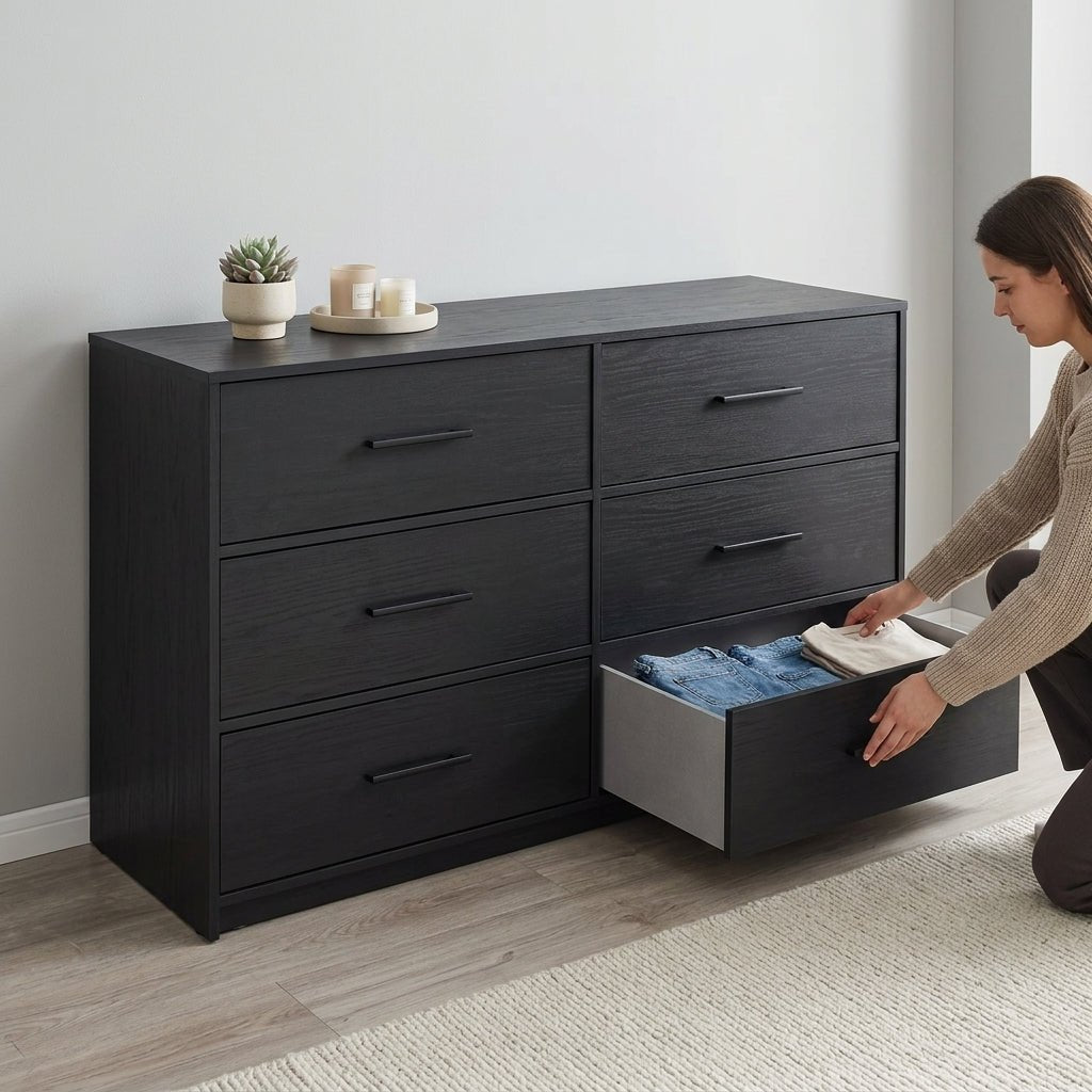 Woman effortlessly organizing folded denim and sweaters into the spacious, extra-large drawer of a modern black bedroom dresser.