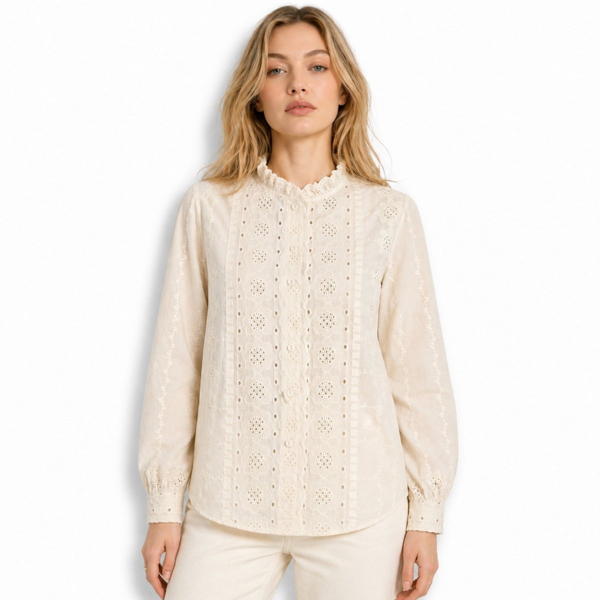 Front view of beautiful woman wearing an beige broderie anglaise long sleeve blouse with ruffled mock neck and floral eyelet embroidery against a white background.