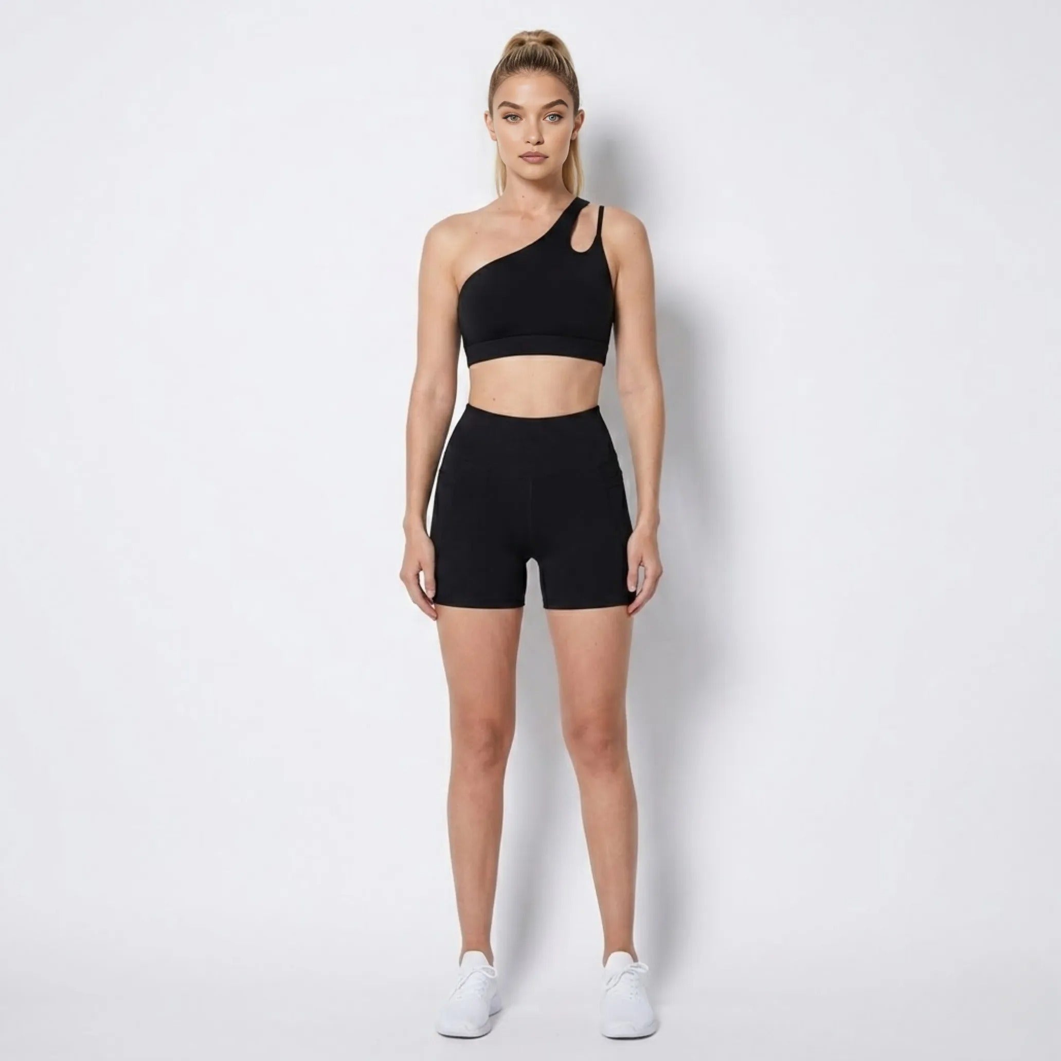 Woman wearing Kouvr black asymmetrical one shoulder activewear set with high waisted biker shorts facing forward