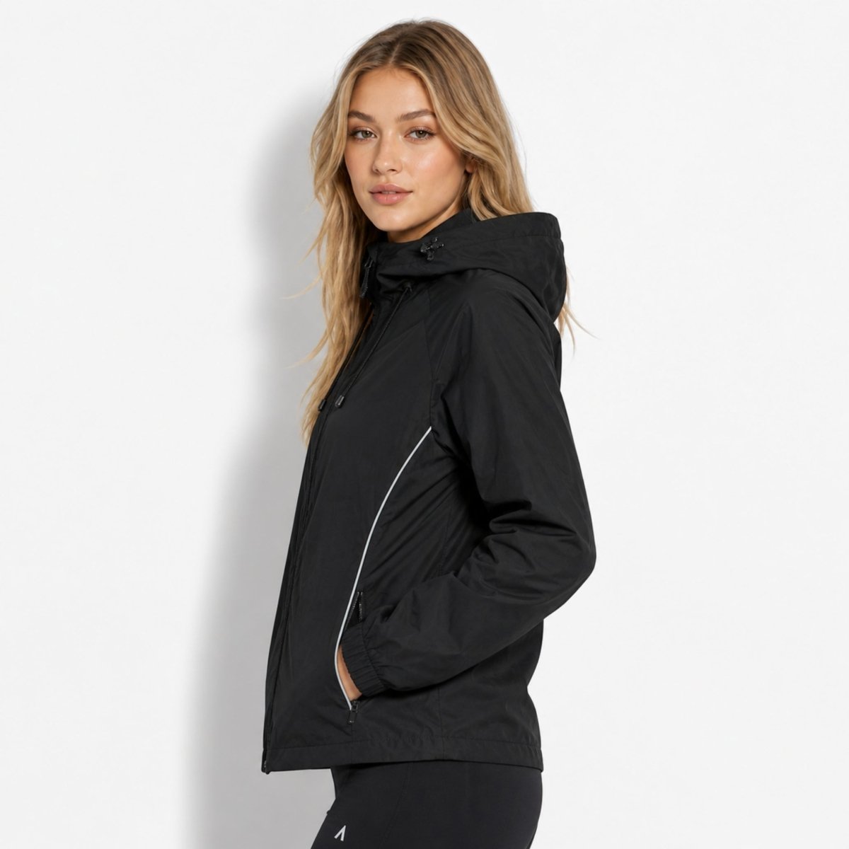 Side profile of woman wearing Kouvr black zip-up windbreaker showing raglan sleeve and adjustable hood.