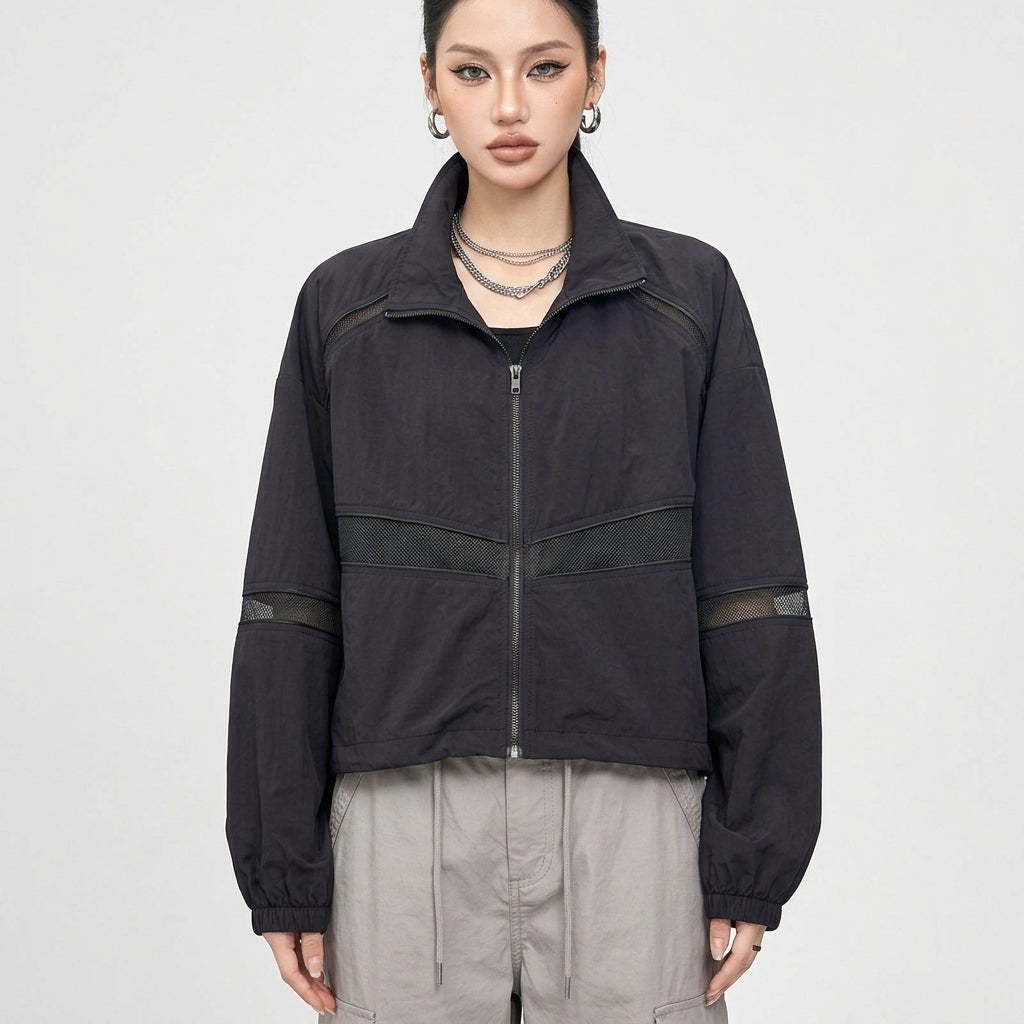 Front view of Kouvr women's black cropped windbreaker jacket with sheer mesh panels and full zip closure on studio model