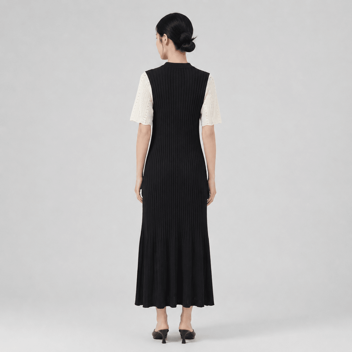 Back view of female model wearing the Kouvr fitted black ribbed sweater dress showing the back silhouette and fluted hem.