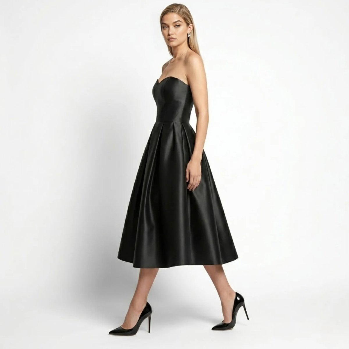 Side profile of model walking in black satin a-line midi dress with strapless sweetheart bodice by Kouvr 