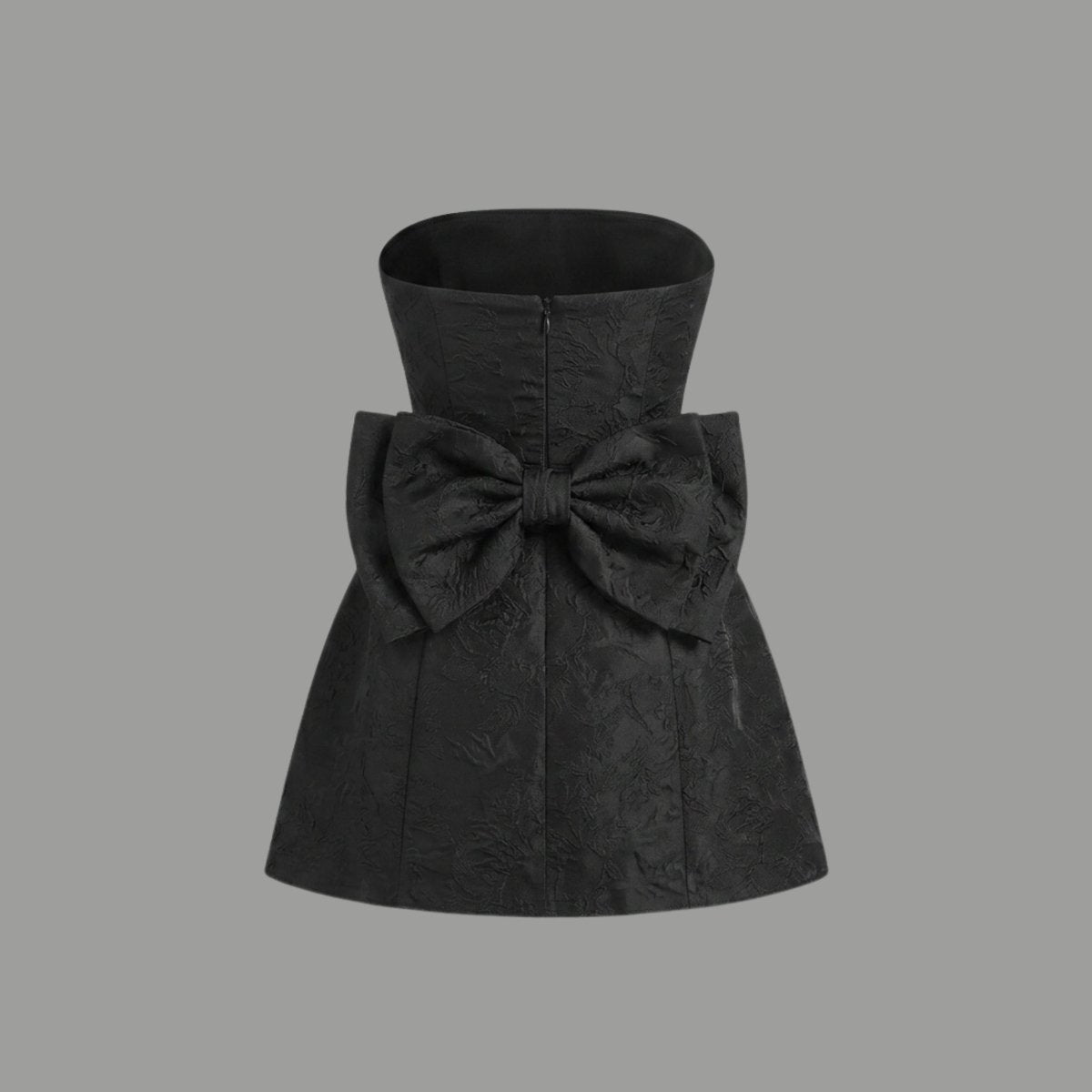 Ghost mannequin back styling of a black mini dress highlighting the oversized attached statement bow and hidden zipper.