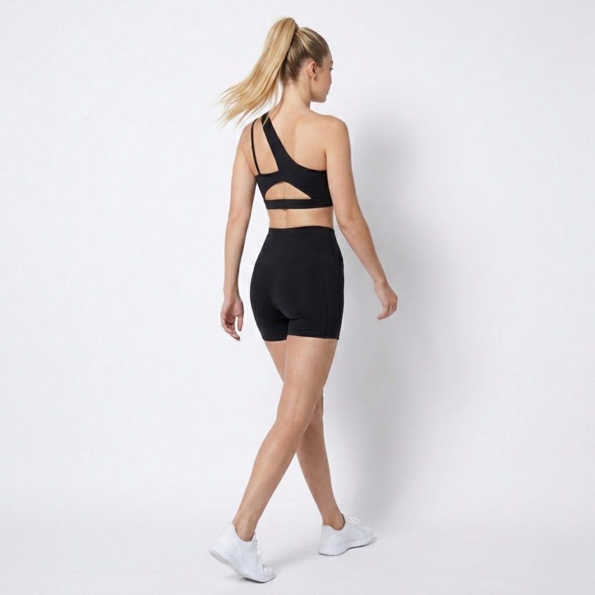 Back view of woman in Kouvr black activewear set featuring an open strappy back sports bra and high waisted shorts 