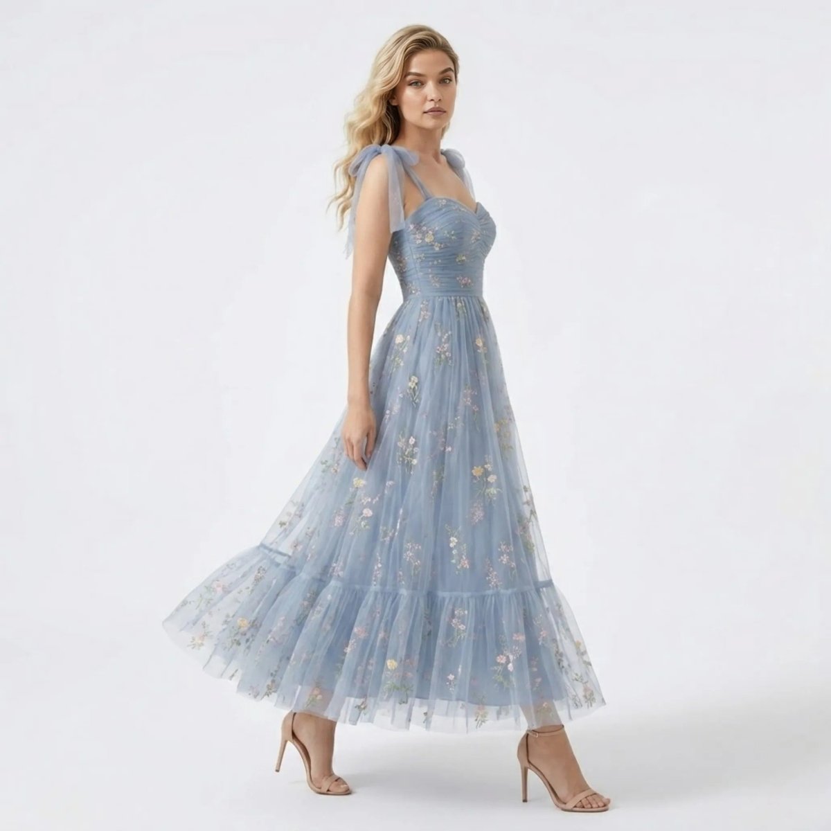 Side angle of a blonde model twirling in the Kouvr blue tulle tiered maxi dress showcasing vibrant floral embroidery and flowy A-line skirt.