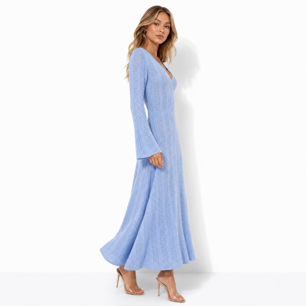 Side angle of a woman modeling a light blue pointelle knit vacation dress highlighting the A-line flared hem and long dramatic bell sleeves.