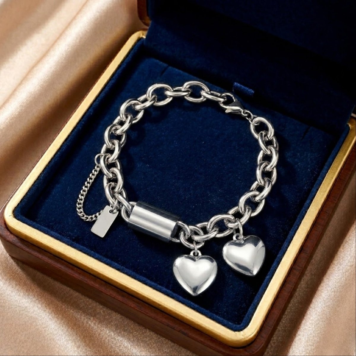 Close-up of a high-shine 18k gold plated chunky chain bracelet with heart and barrel charms on gold silk fabric.