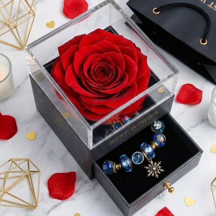 Angled shot of a classic red preserved rose in a clear-top display box with the drawer pulled out to show a blue charm bracelet.