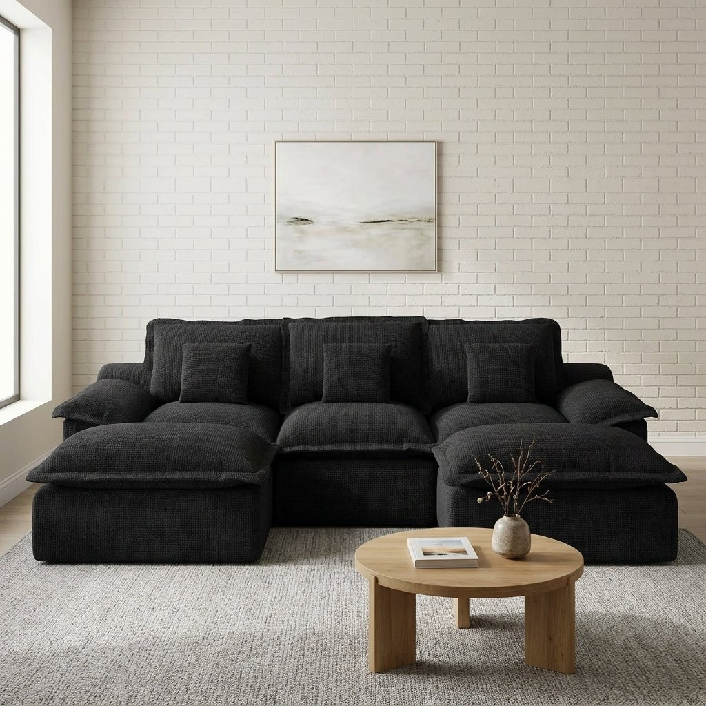 A woman and a goldendoodle dog relaxing on a comfortable, large black modular sectional sofa in a bright home.