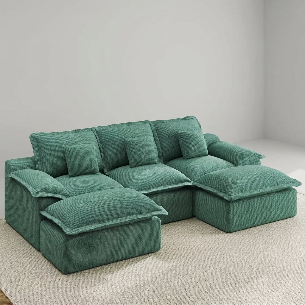 A woman working on a laptop while lounging on a comfortable green modular sofa with a cat nearby.