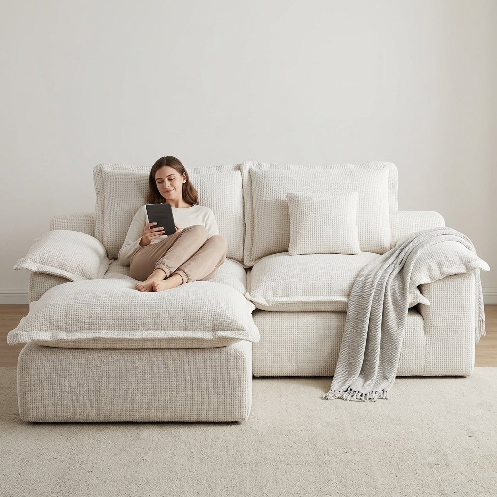 A woman lounging comfortably on a modular cream chaise sofa while using an e-reader in a bright room.