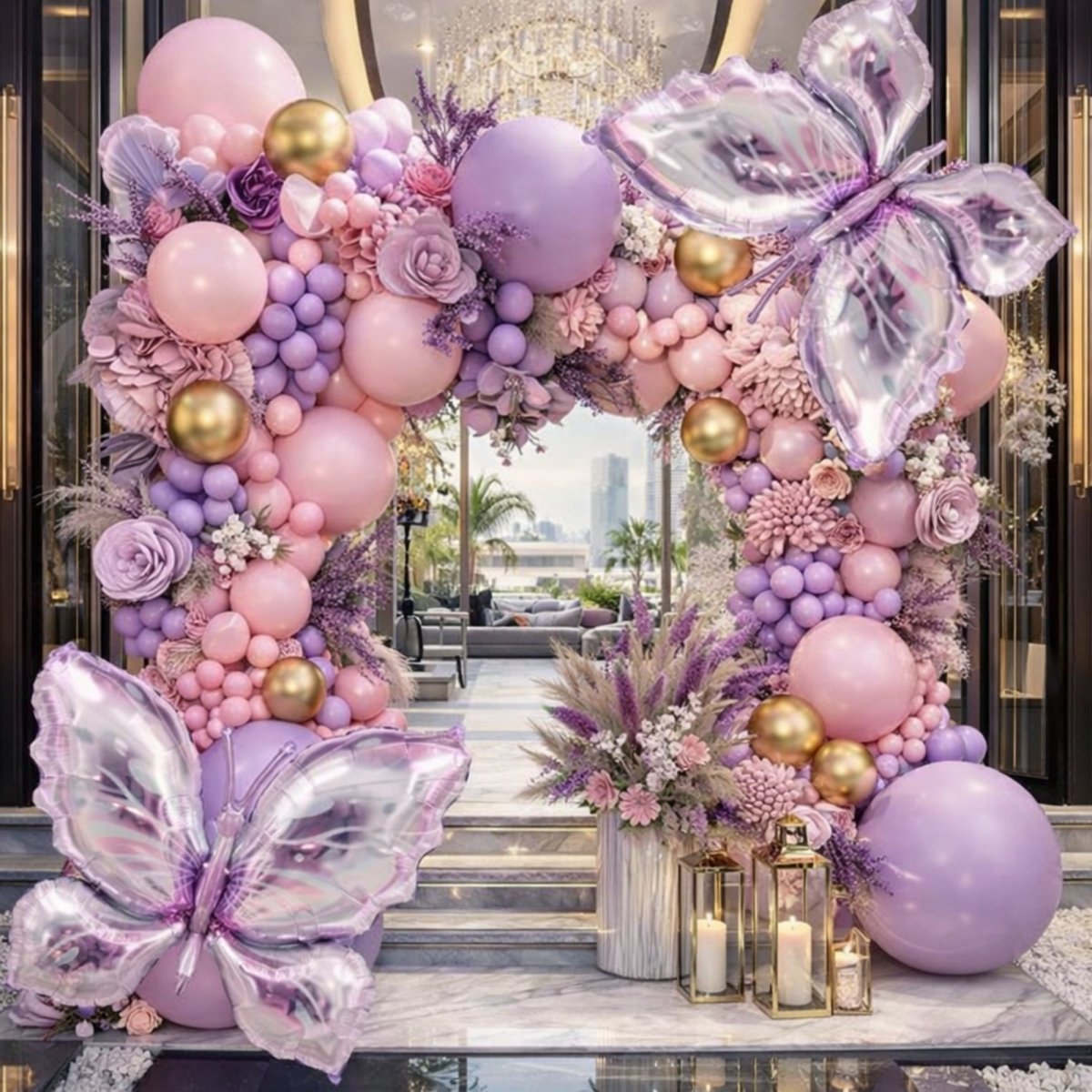 A complete outdoor tablescape and party setup with a lavender butterfly balloon arch, matching floral centerpieces, a multi-tier cake, and string lights overlooking the ocean for a high-end birthday.
