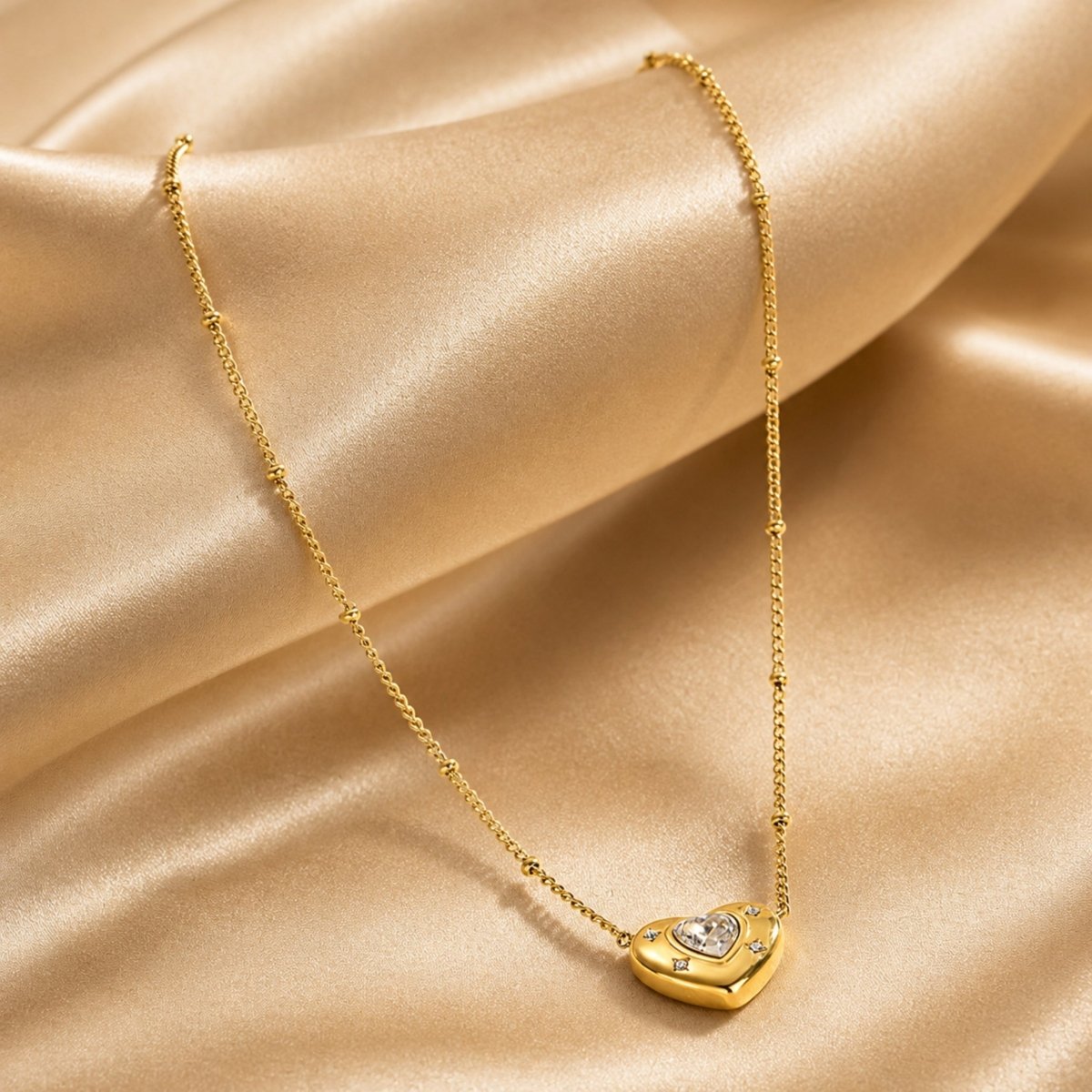 Gold 304 stainless steel heart pendant necklace resting elegantly on draped champagne satin material.