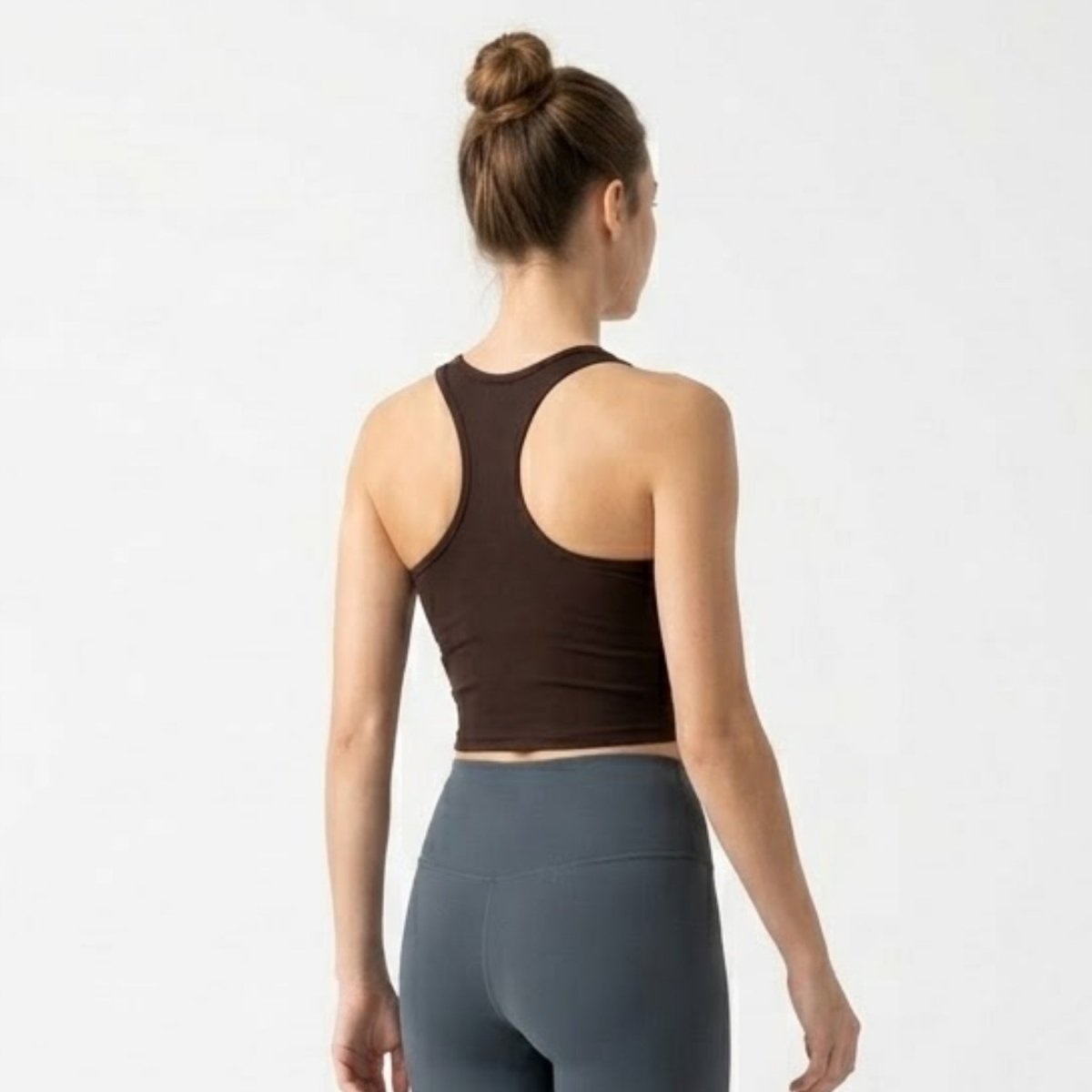 Woman wearing a dark brown racerback activewear crop top showing back shoulder detailing.