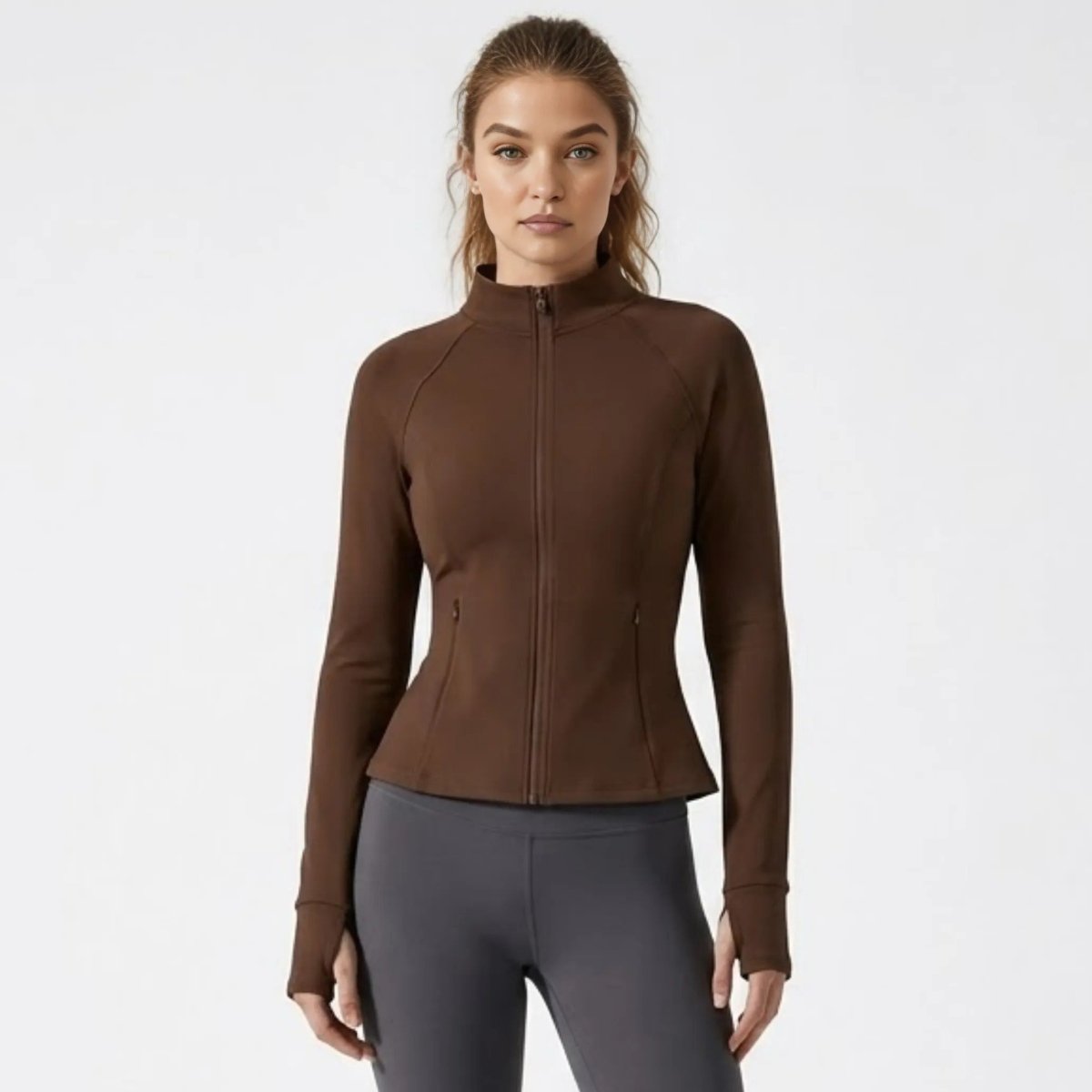 Front view of female model wearing Kouvr dark brown fitted zip-up athletic jacket with grey leggings
