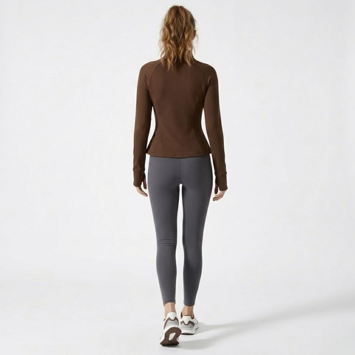 Back full body lifestyle shot of female model walking in Kouvr brown zip-up activewear jacket