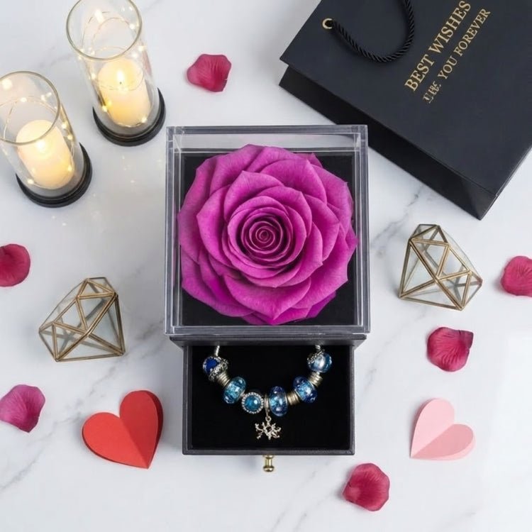 Overhead photo of a vibrant purple eternal rose centerpiece in a black square box on a marble table with scattered rose petals.