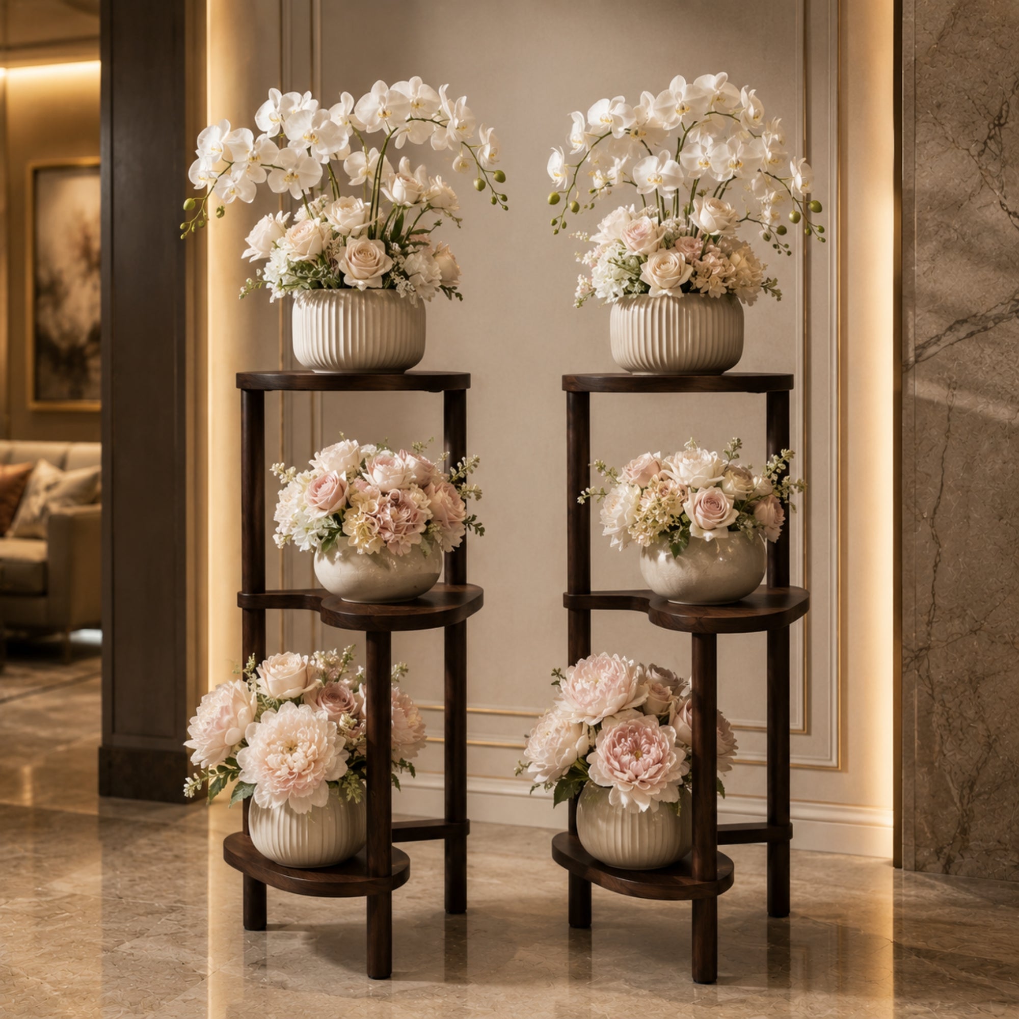 Twin dark wood 3-tier display shelves featuring elaborate white and pink floral orchid arrangements in a luxury entryway.
