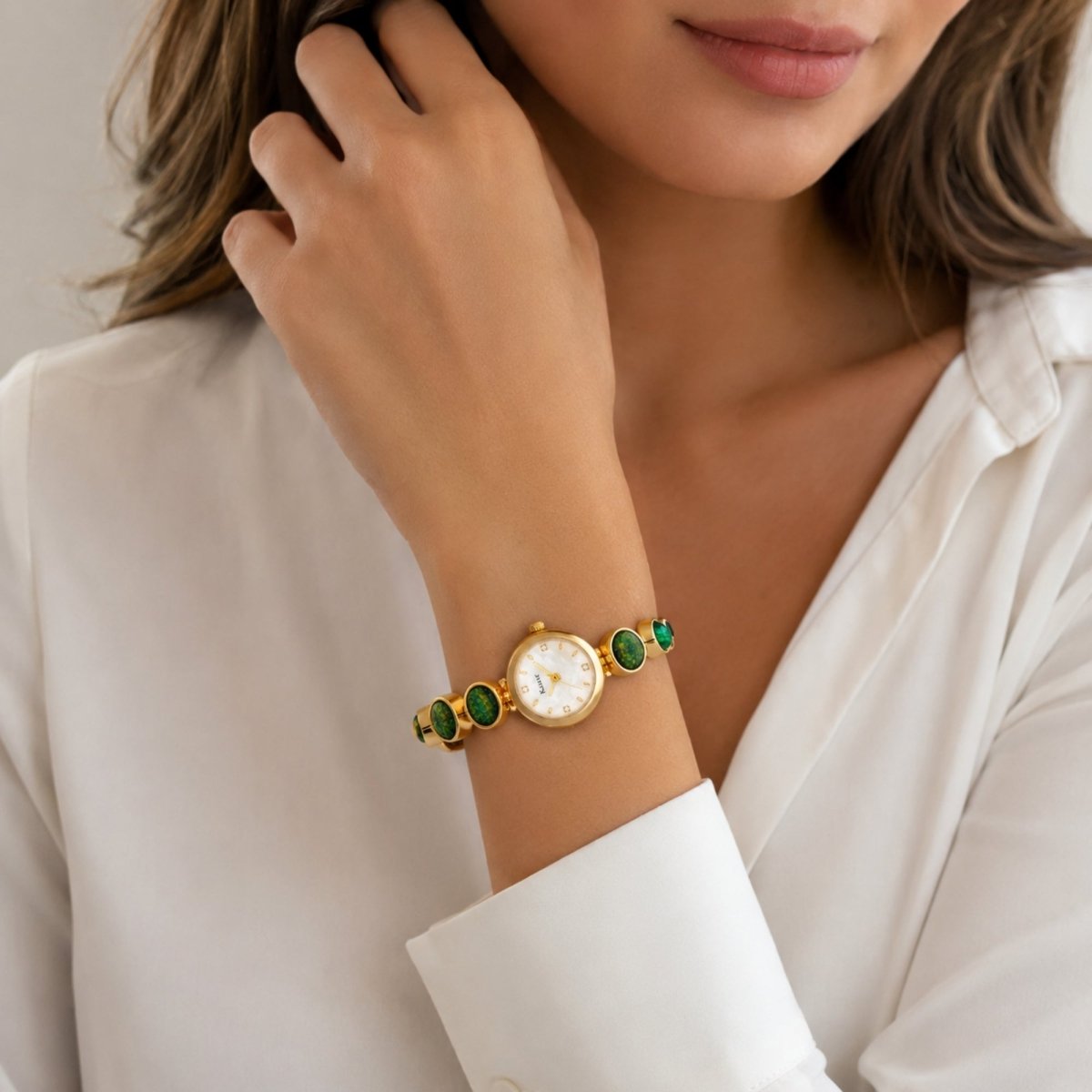 Close up of a sophisticated woman wearing a classic white blouse styling the gold Kouvr vintage green stone bracelet watch on her wrist.