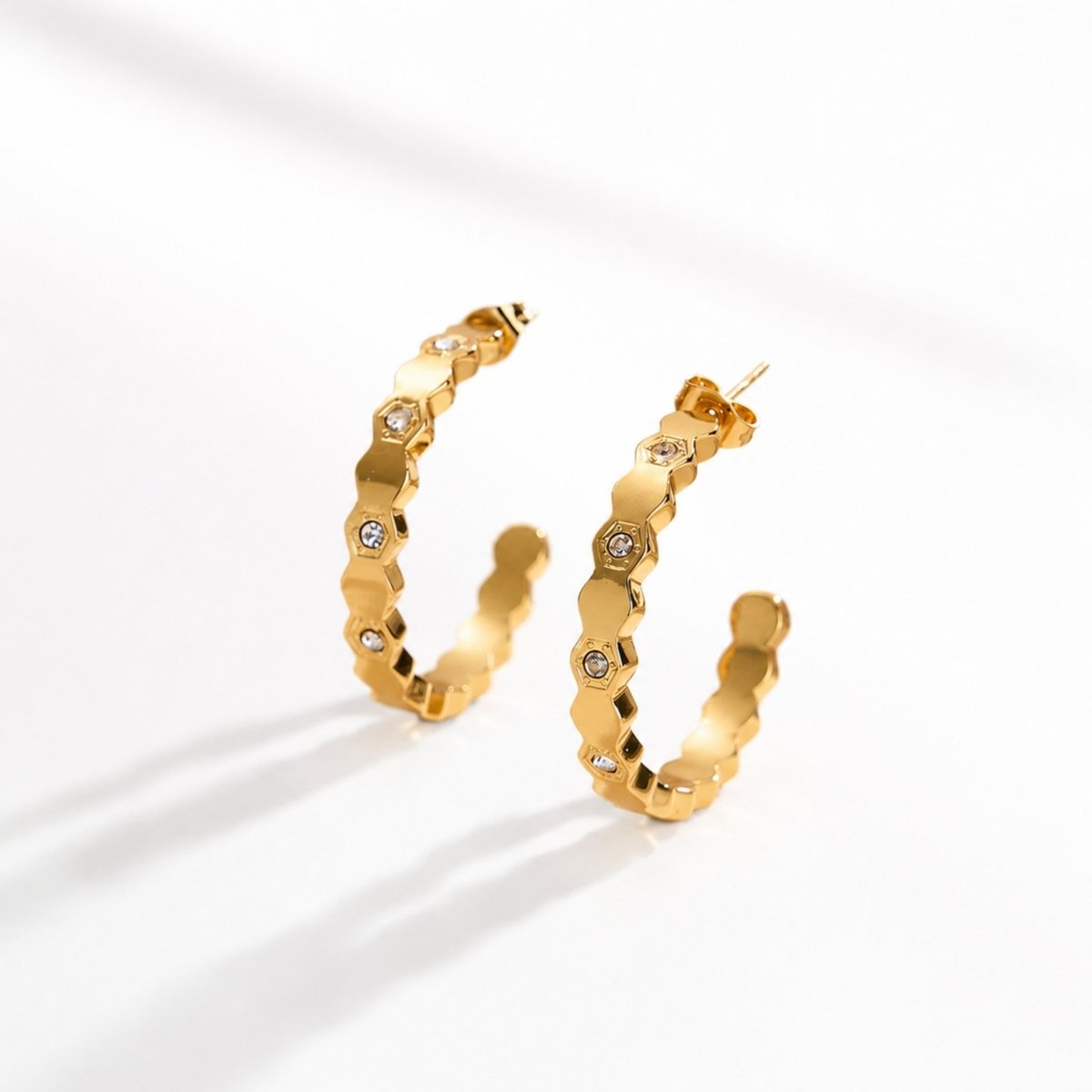 Pair of 18k gold plated geometric hexagon hoop earrings with embedded crystals standing upright on a seamless white surface