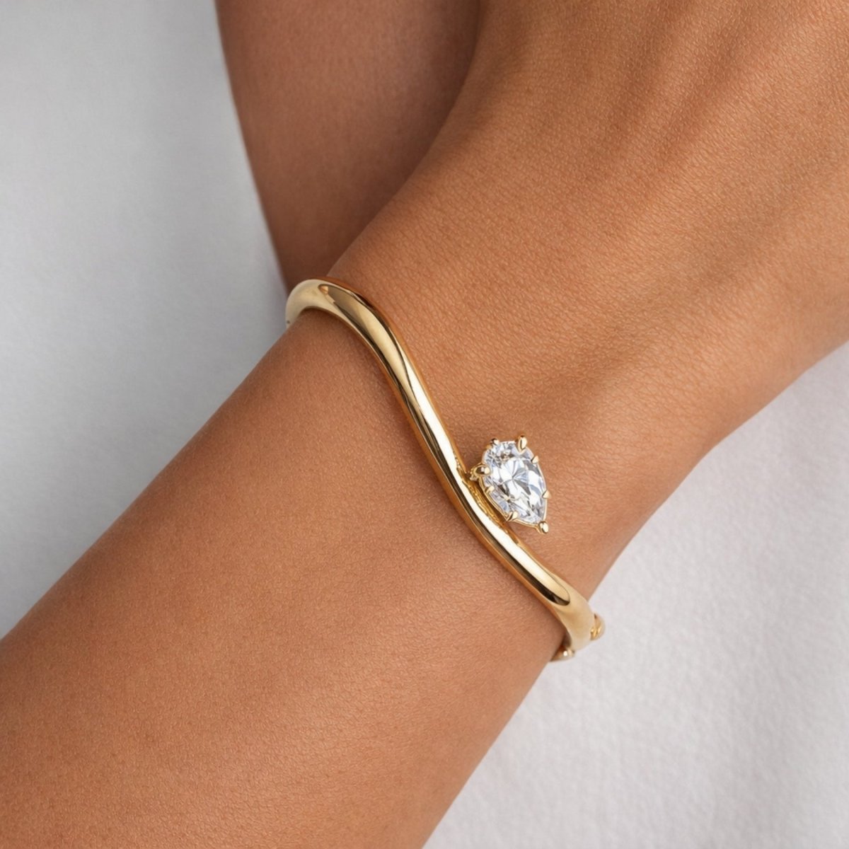 A model's wrist wearing the Kouvr Yelena gold teardrop crystal bangle against a soft white shirt.