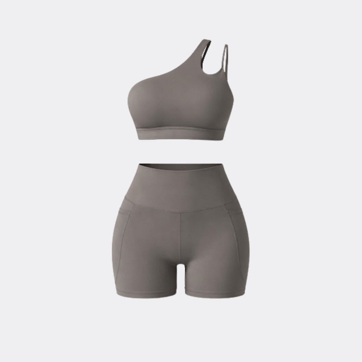 Flat lay studio shot of Kouvr grey two piece workout outfit featuring asymmetrical top and pocket biker shorts.
